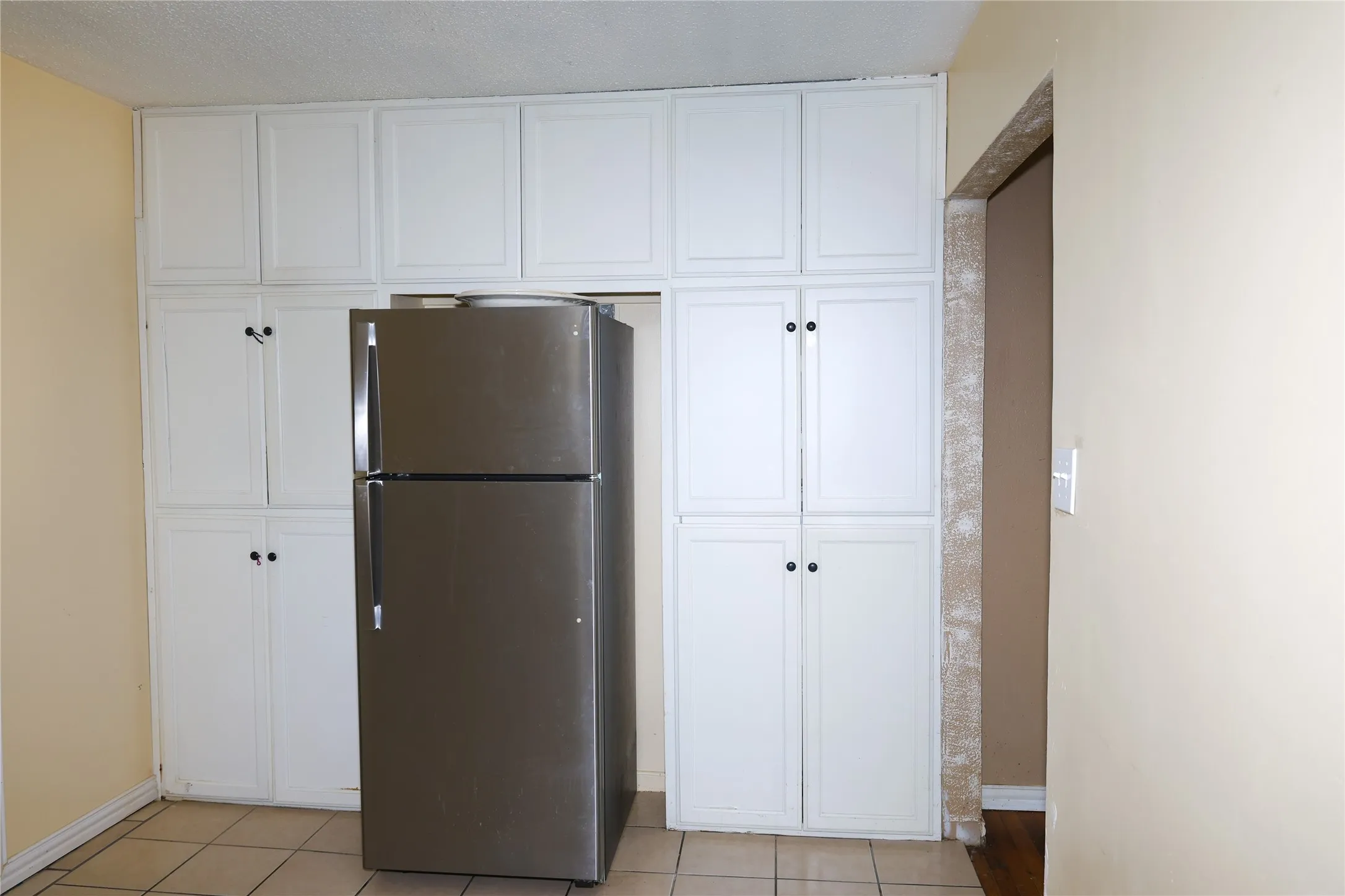 Kitchen area featuring extensive white cabinetry, a built-in refrigerator alcove, tiled flooring, and neutral wall paint