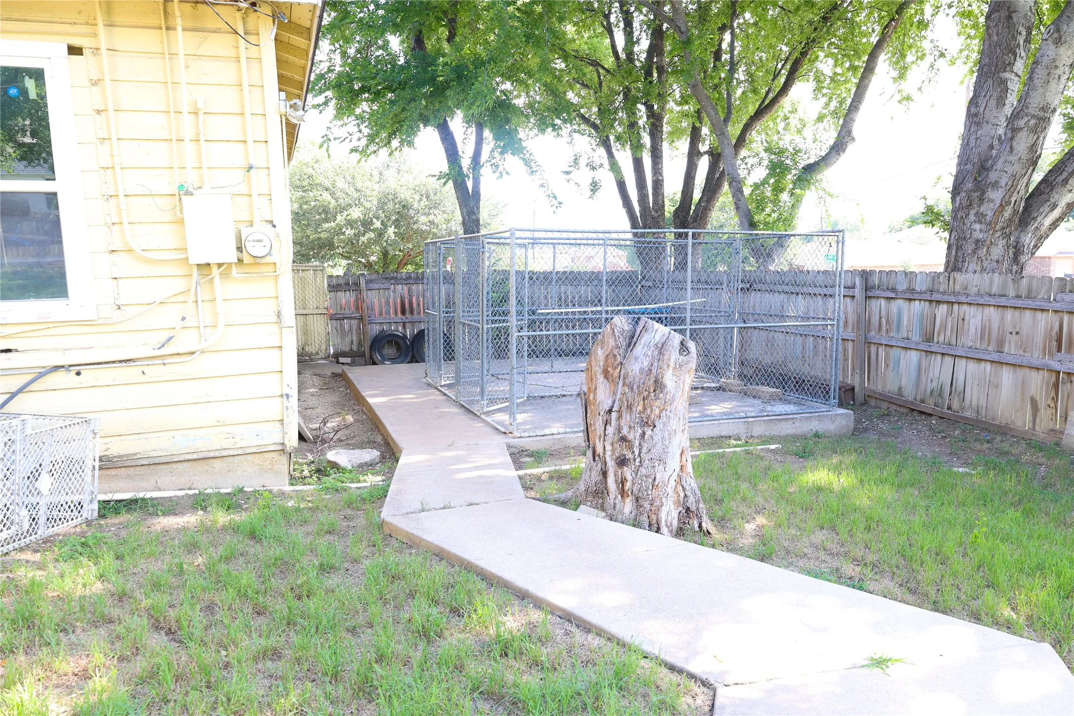 Fenced backyard area featuring a concrete pad, chain-link enclosure, and a wood privacy fence