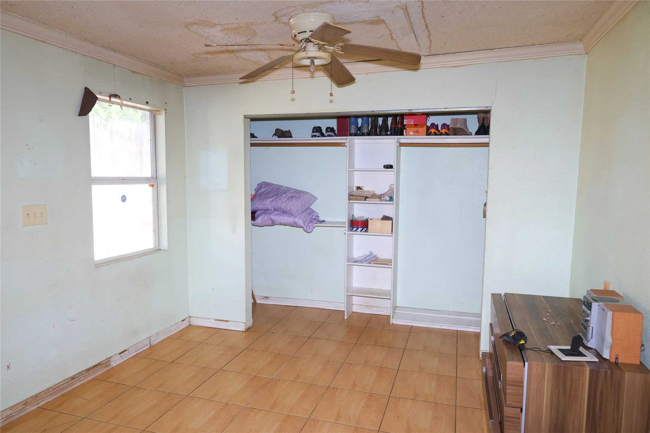 Room featuring wood-finish tile flooring, a built-in closet with shelving, a ceiling fan, crown molding, and a window for natural light