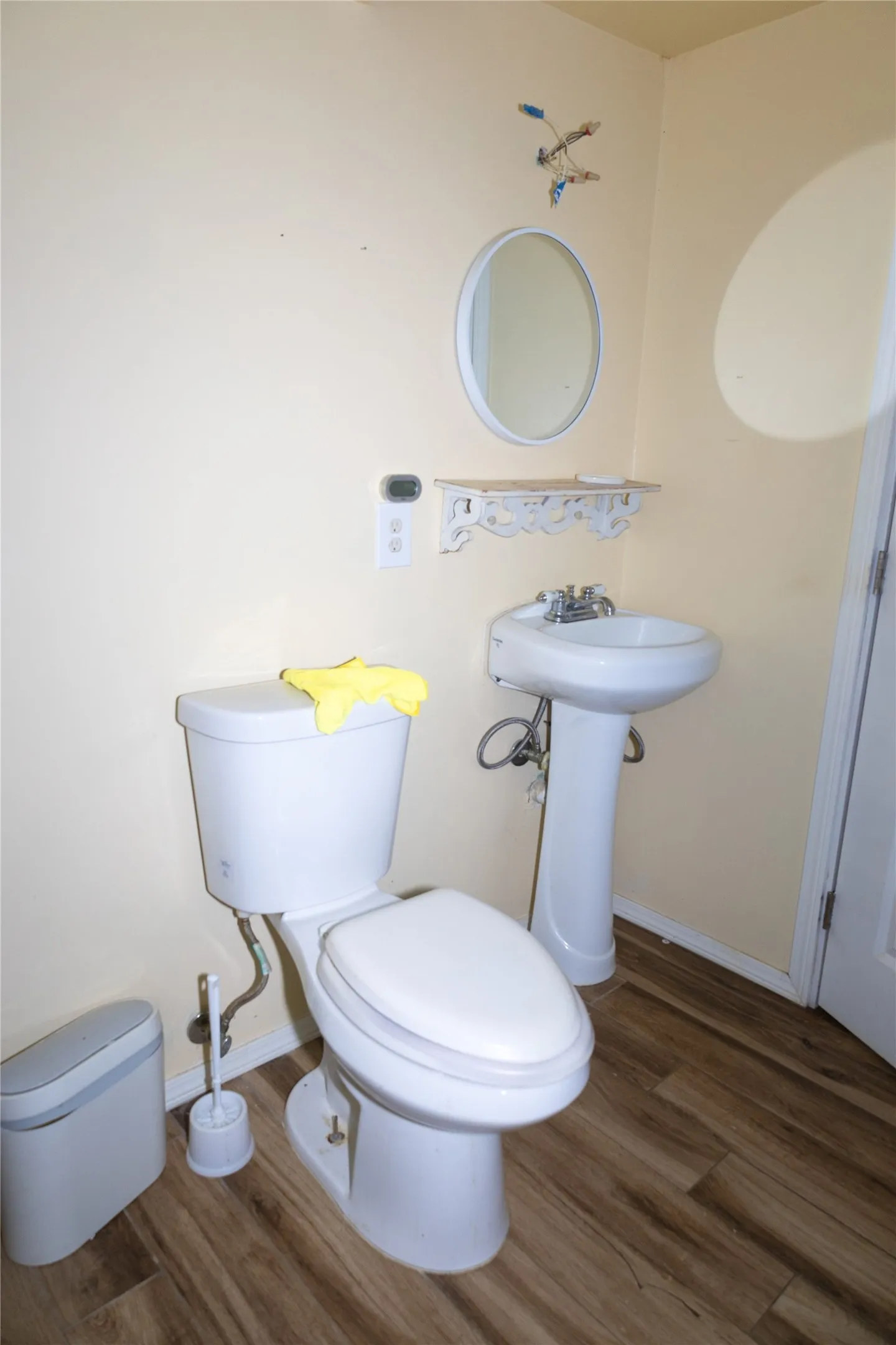 Bathroom featuring wood-finish flooring, a white pedestal sink, and a white toilet