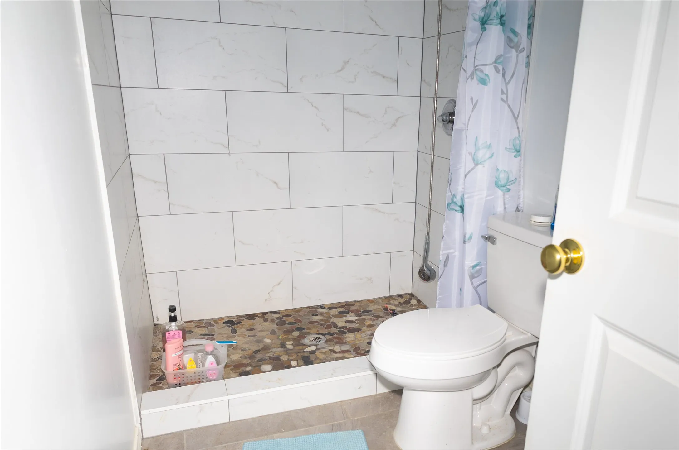 Walk-in shower featuring white subway tile surround and a pebble-finish base