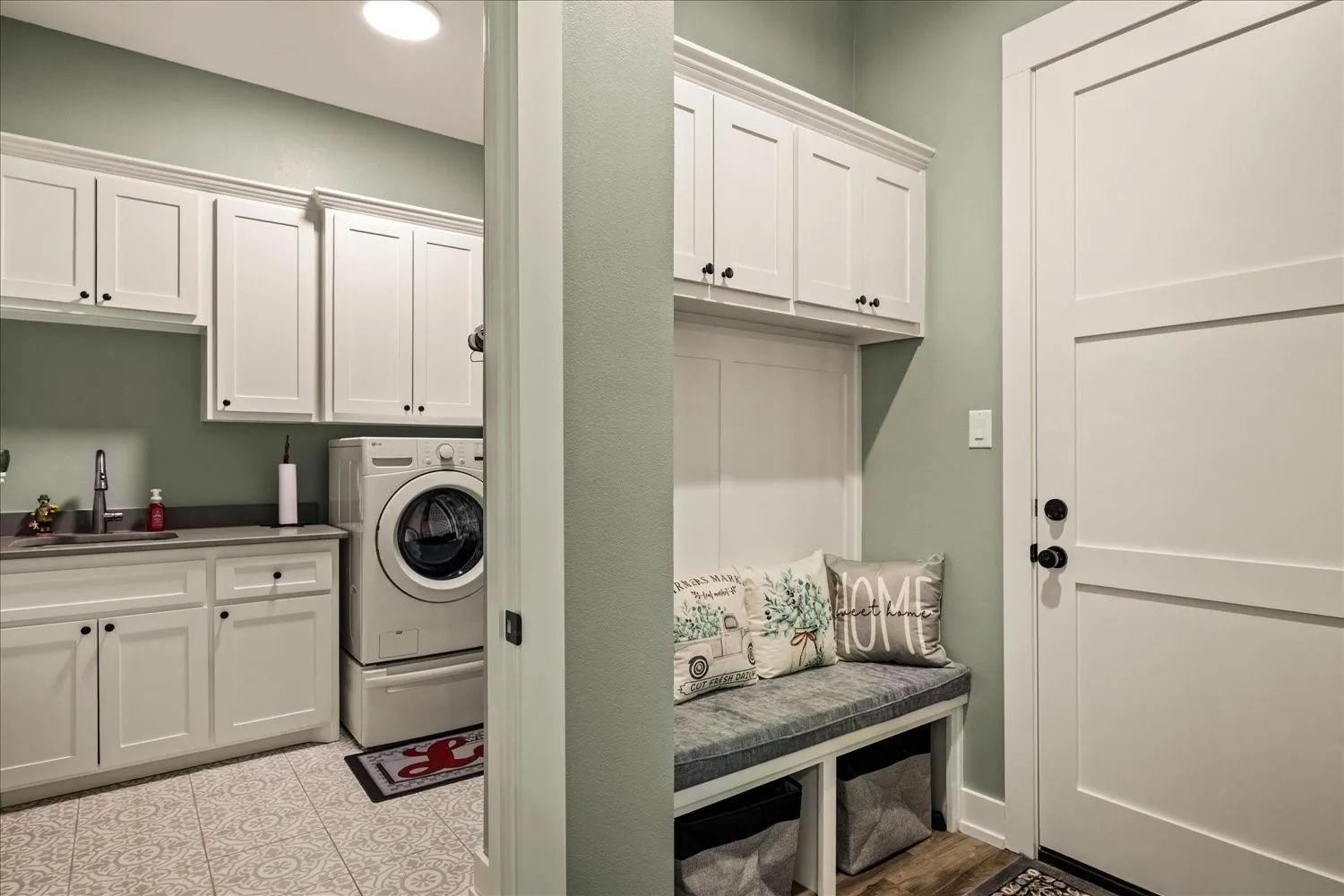 Laundry and mudroom combination featuring a built-in bench with storage, overhead cabinetry, a utility sink, and patterned floor tile