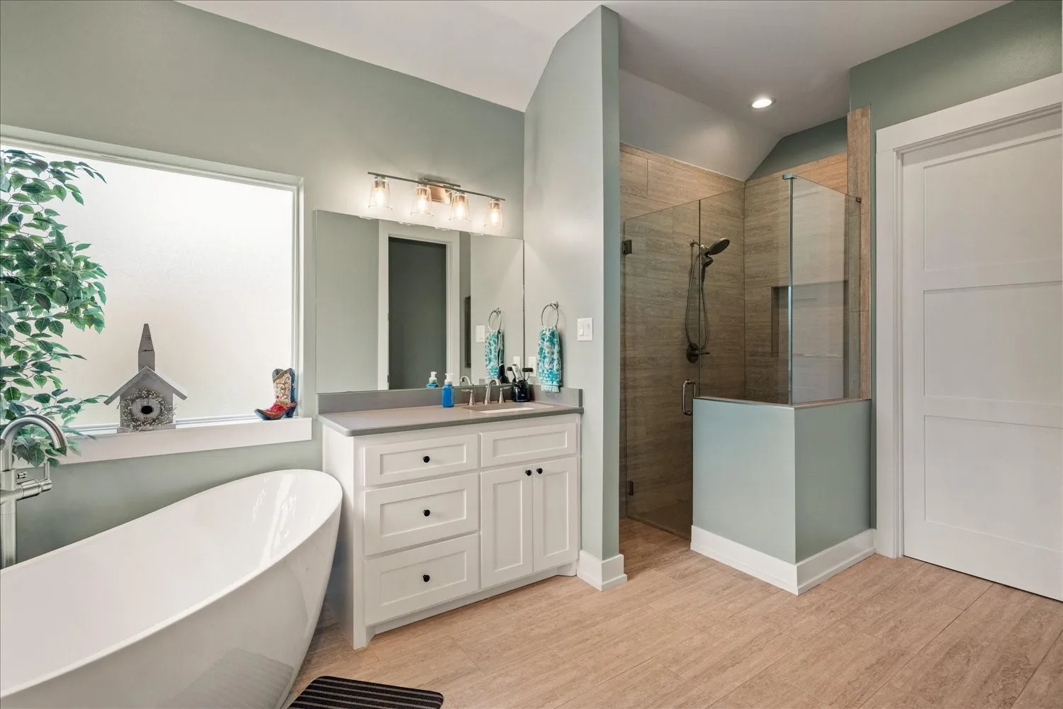 Bathroom featuring a freestanding soaking tub, a double vanity with ample storage, a glass-enclosed shower with tiled walls, and wood-finish flooring