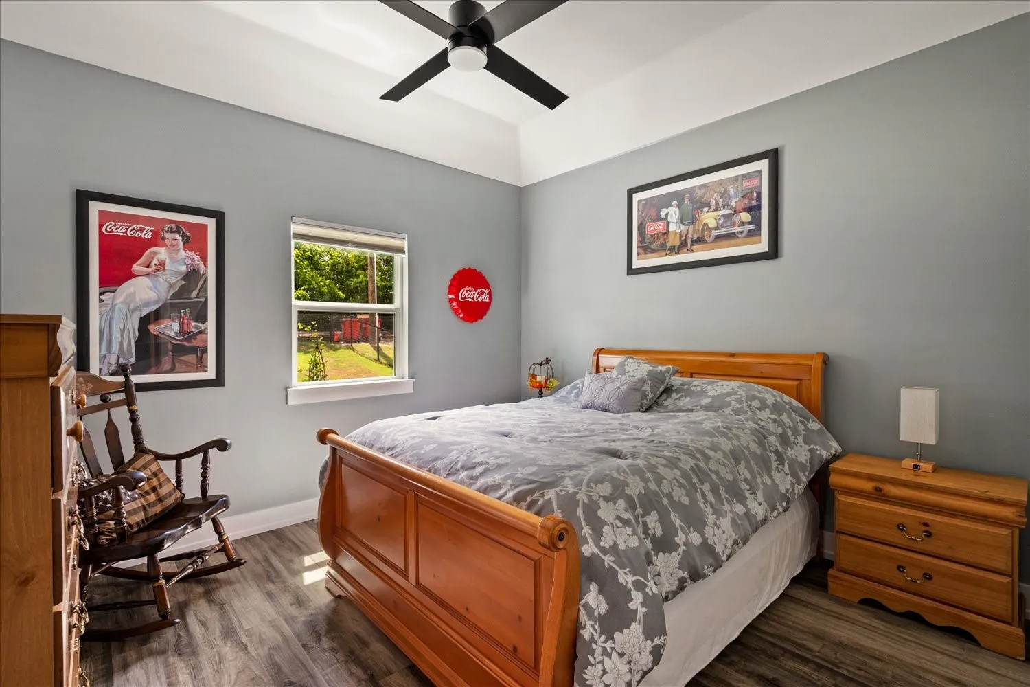 Bedroom featuring vaulted tray ceiling, a ceiling fan, a window with outdoor landscaping, and wood-finish flooring