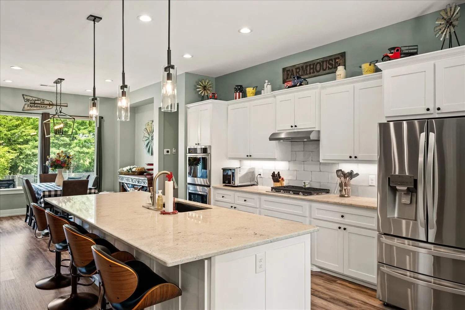 Open-concept kitchen featuring an expansive island with seating, pendant lighting, white cabinetry, stainless steel appliances, and wood-finish flooring