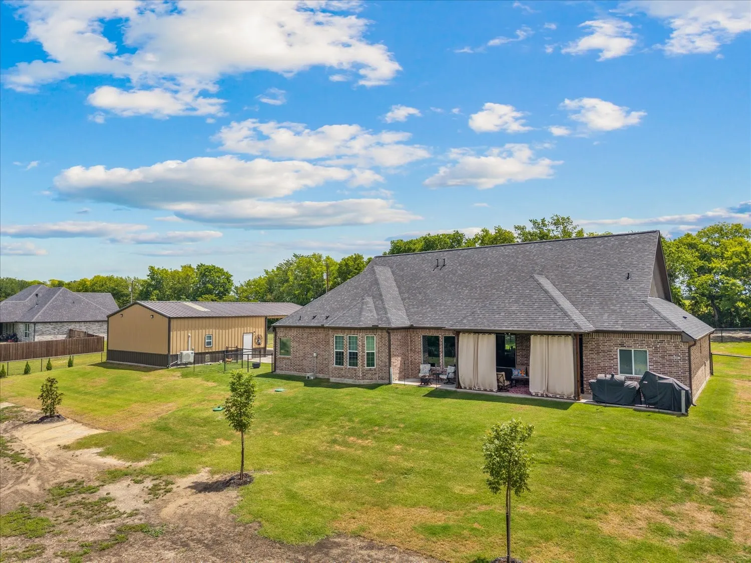 Brick exterior home with a charcoal shingle roof, featuring an expansive green lawn and a large metal outbuilding