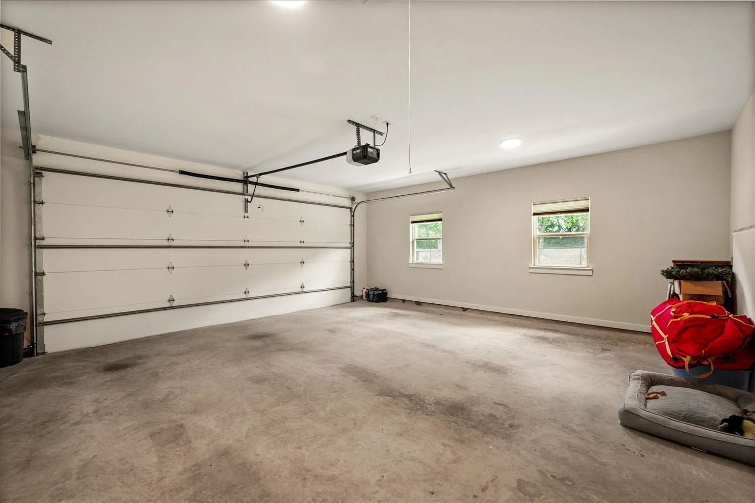 Spacious garage with a sectional overhead door, automatic opener, two windows, and concrete flooring