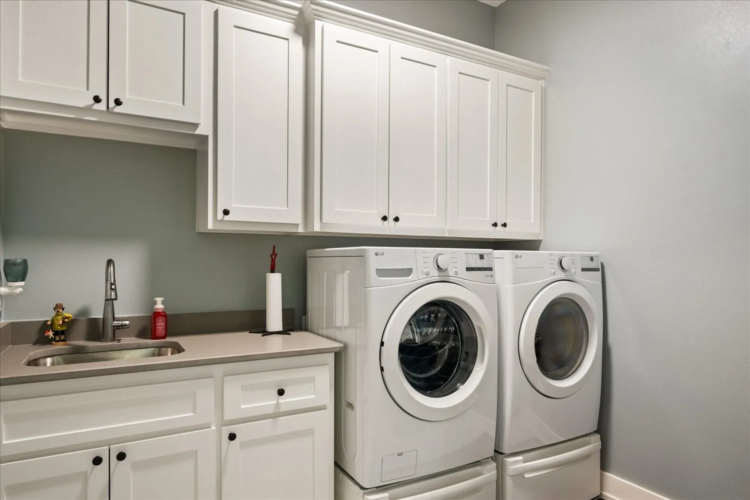 Laundry area featuring white shaker-style cabinetry, a built-in stainless steel sink, a modern faucet, and durable countertop space