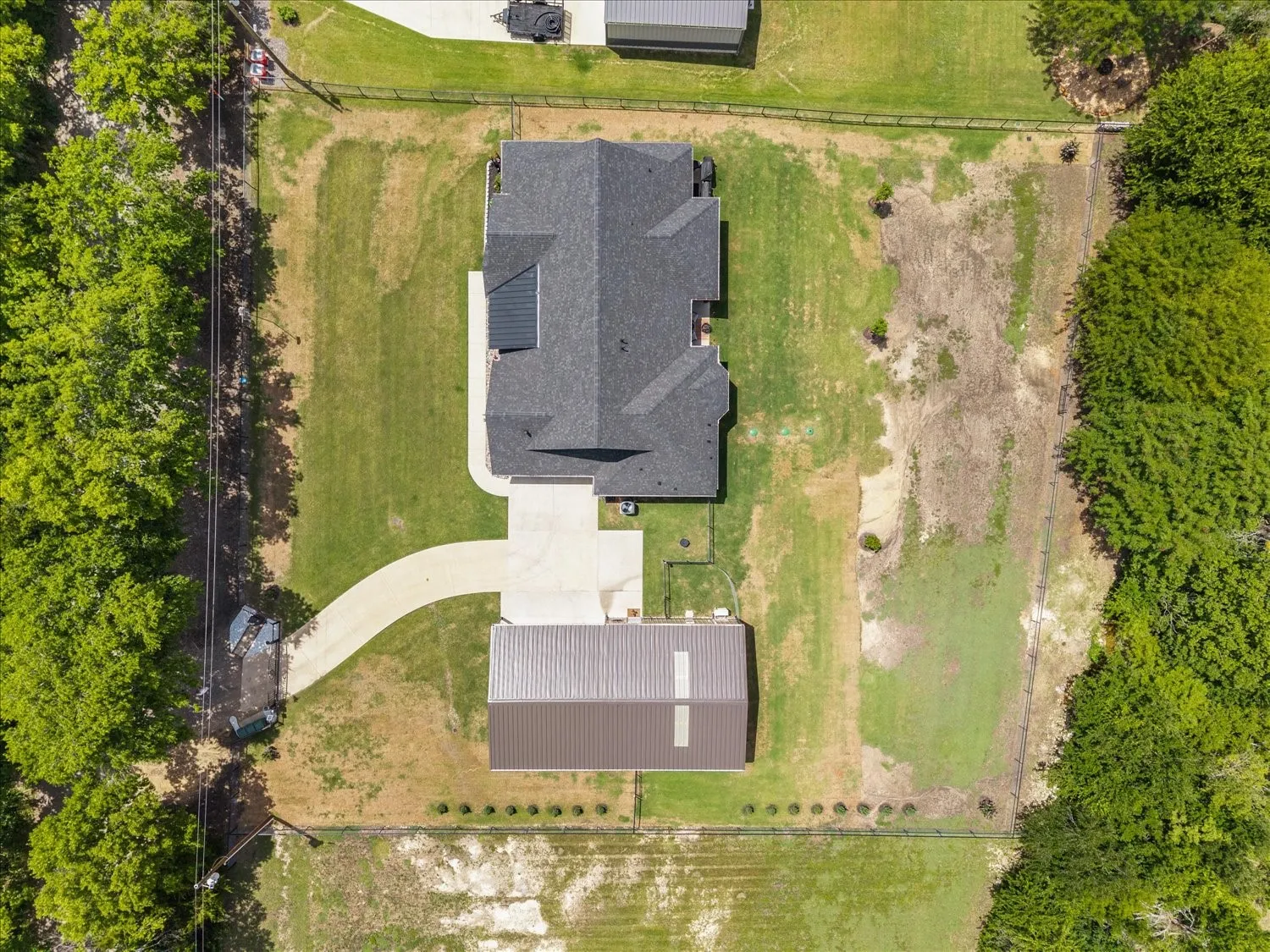 Aerial property view featuring a residence with a dark shingle roof, a detached metal-roofed auxiliary building, an asphalt driveway, and expansive grassed areas