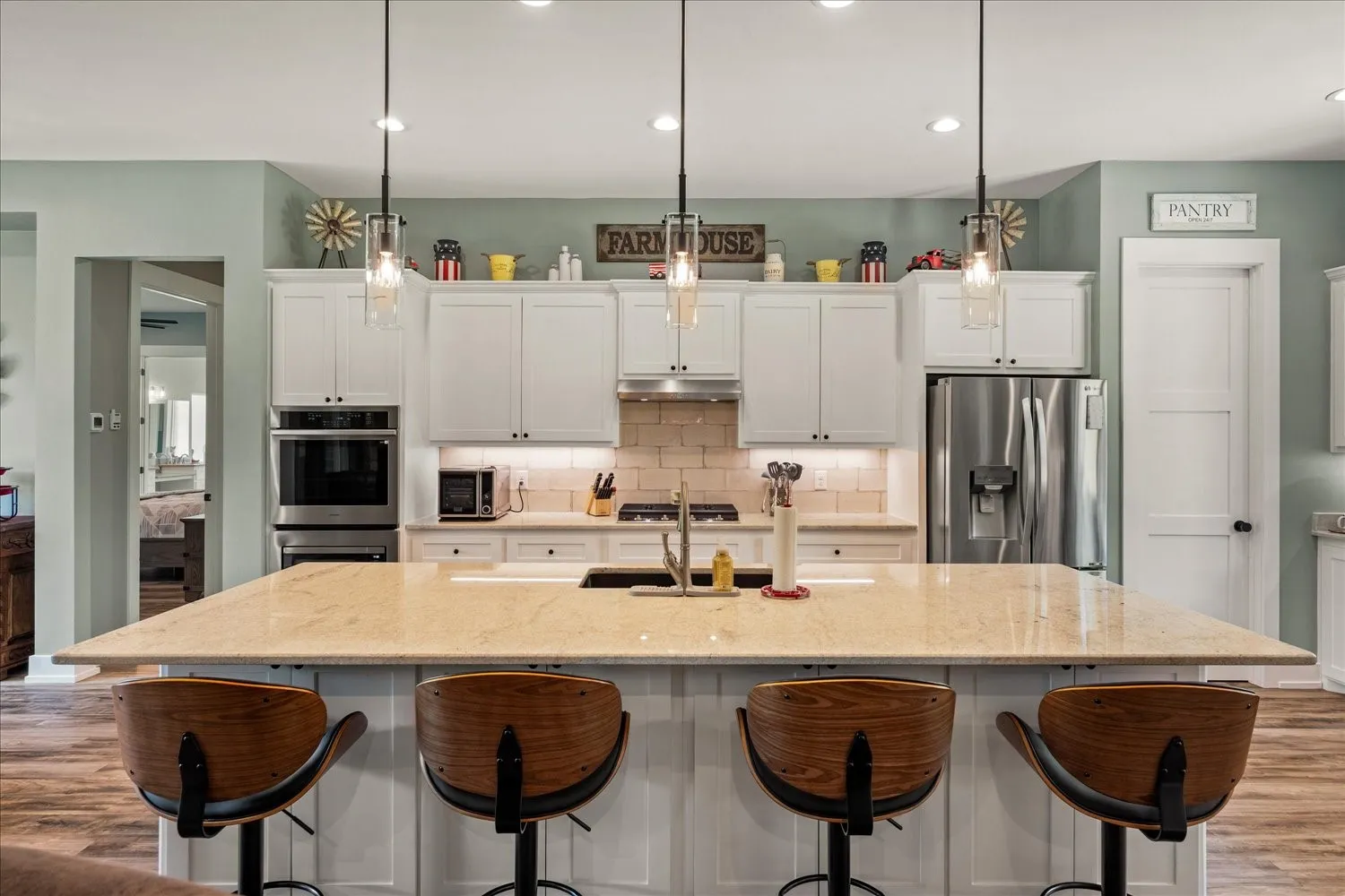 Expansive kitchen island featuring a light-toned countertop, under-cabinet lighting, a built-in oven, and a stainless steel refrigerator