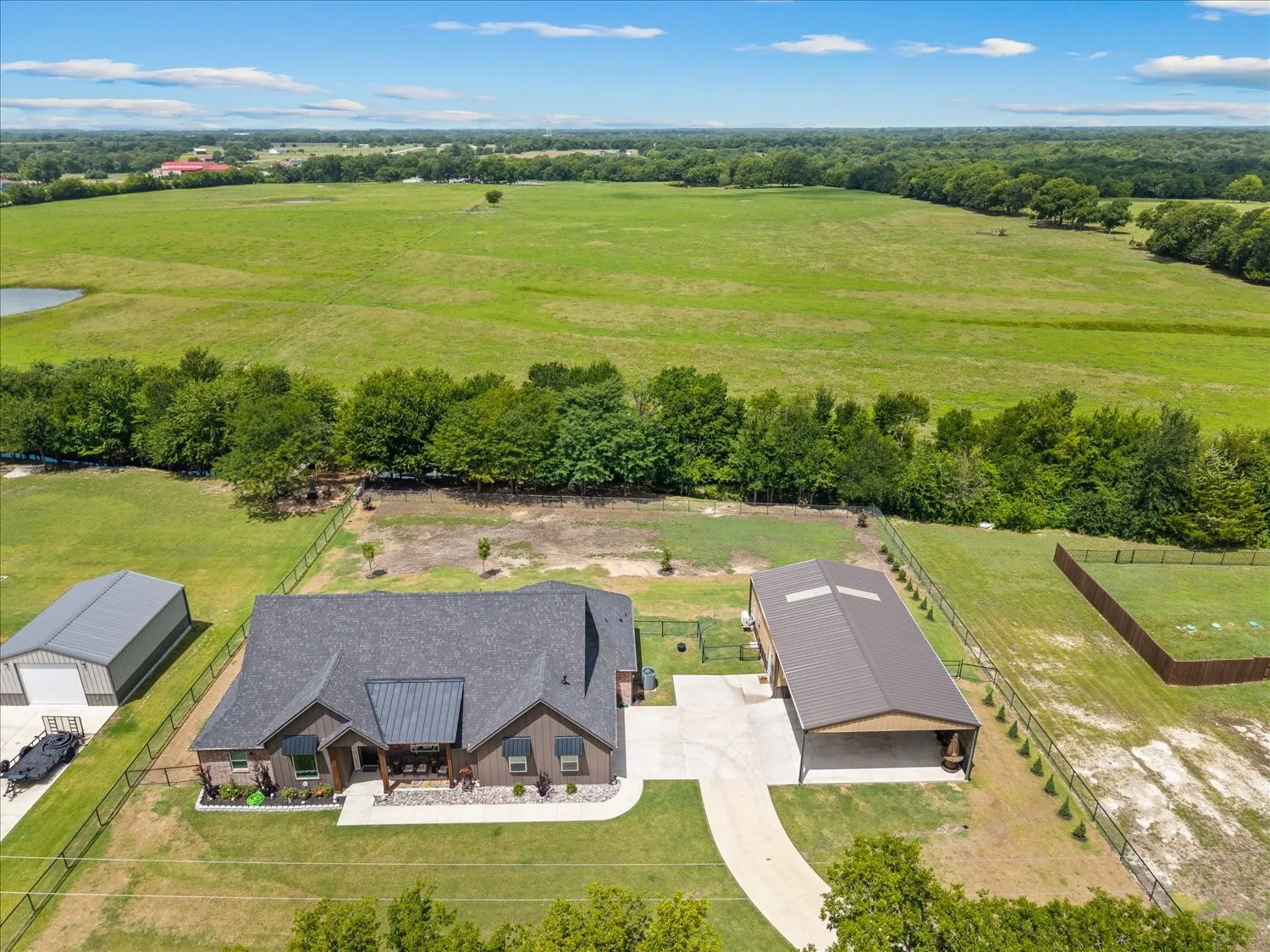 Expansive property featuring a single-story residence, a large detached garage/workshop, a separate metal barn, and extensive green space