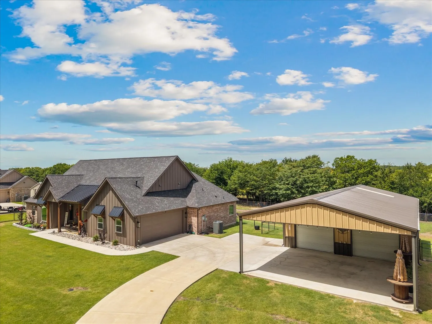 Expansive property featuring a brown siding and brick exterior residence with a dark shingle roof, a two-car garage, and a long concrete driveway