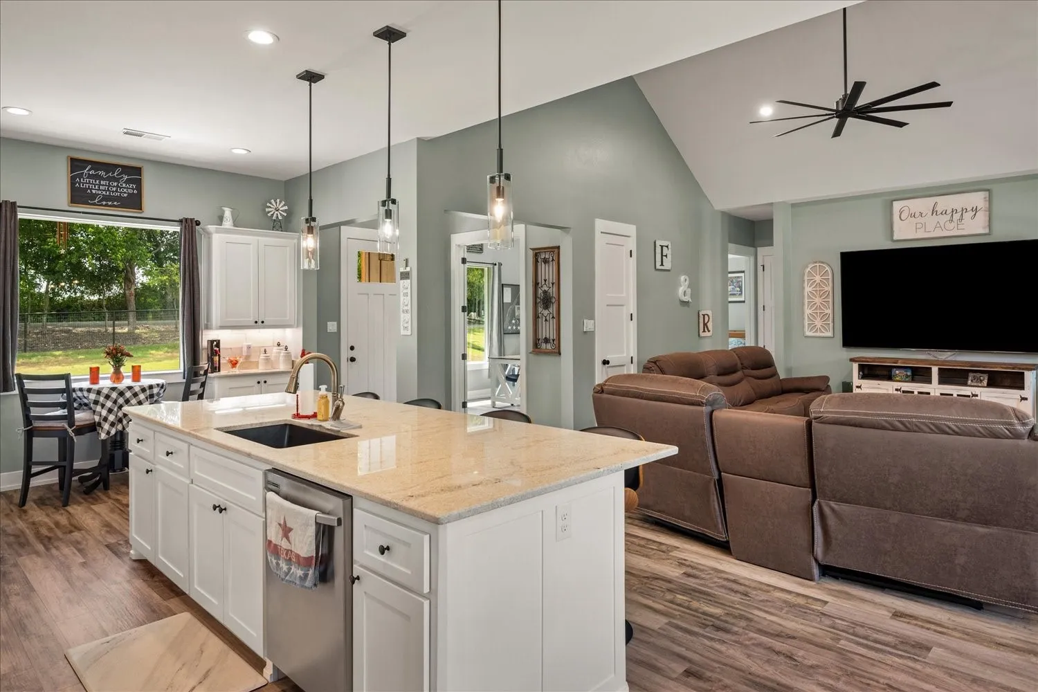 Open-concept living space featuring a central kitchen island with light-toned countertop, wood-finish flooring, white cabinetry, and recessed lighting