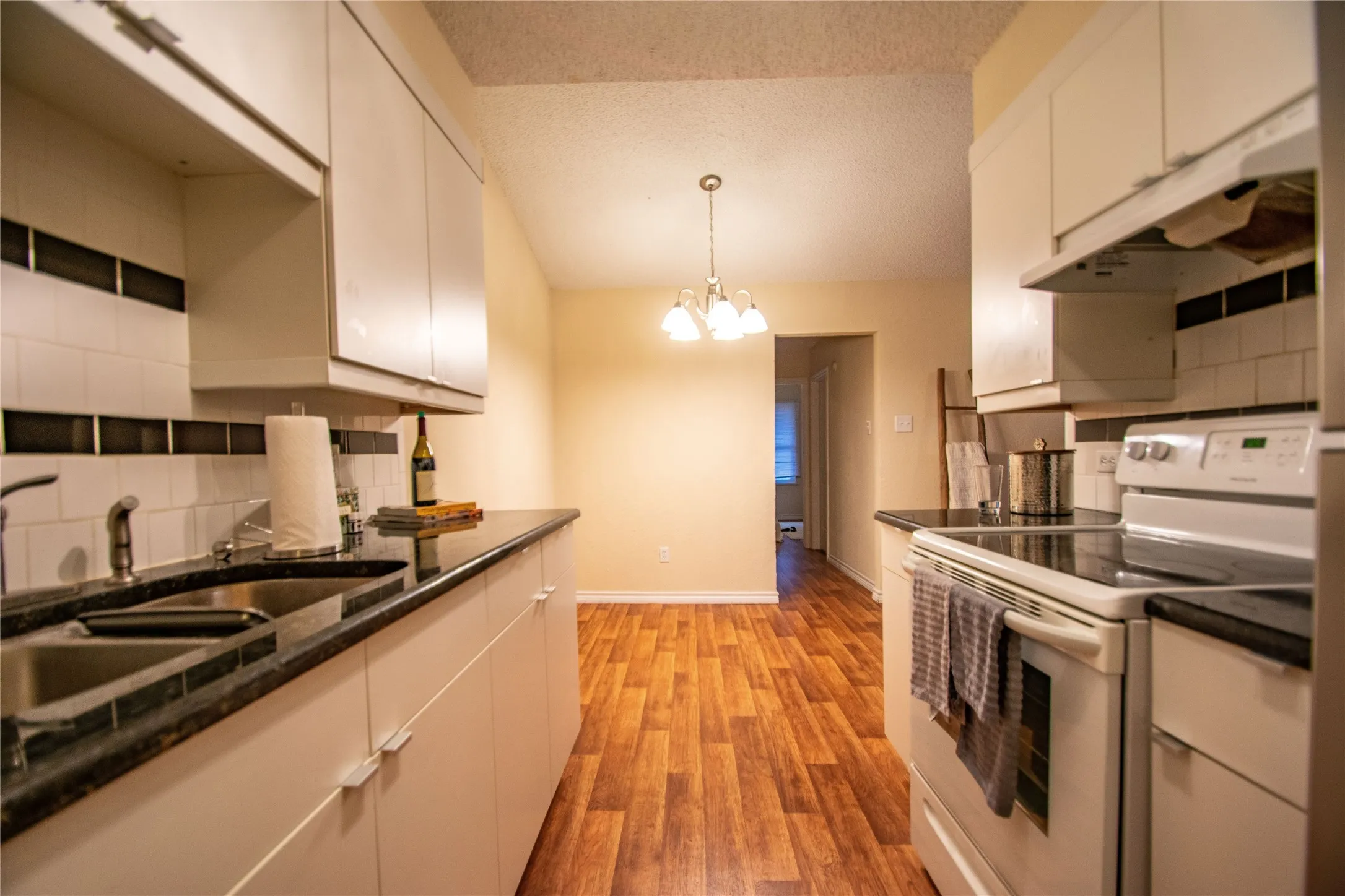 Kitchen with light hardwood / wood-style flooring, white cabinetry, backsplash, a notable chandelier, and white range with electric stovetop