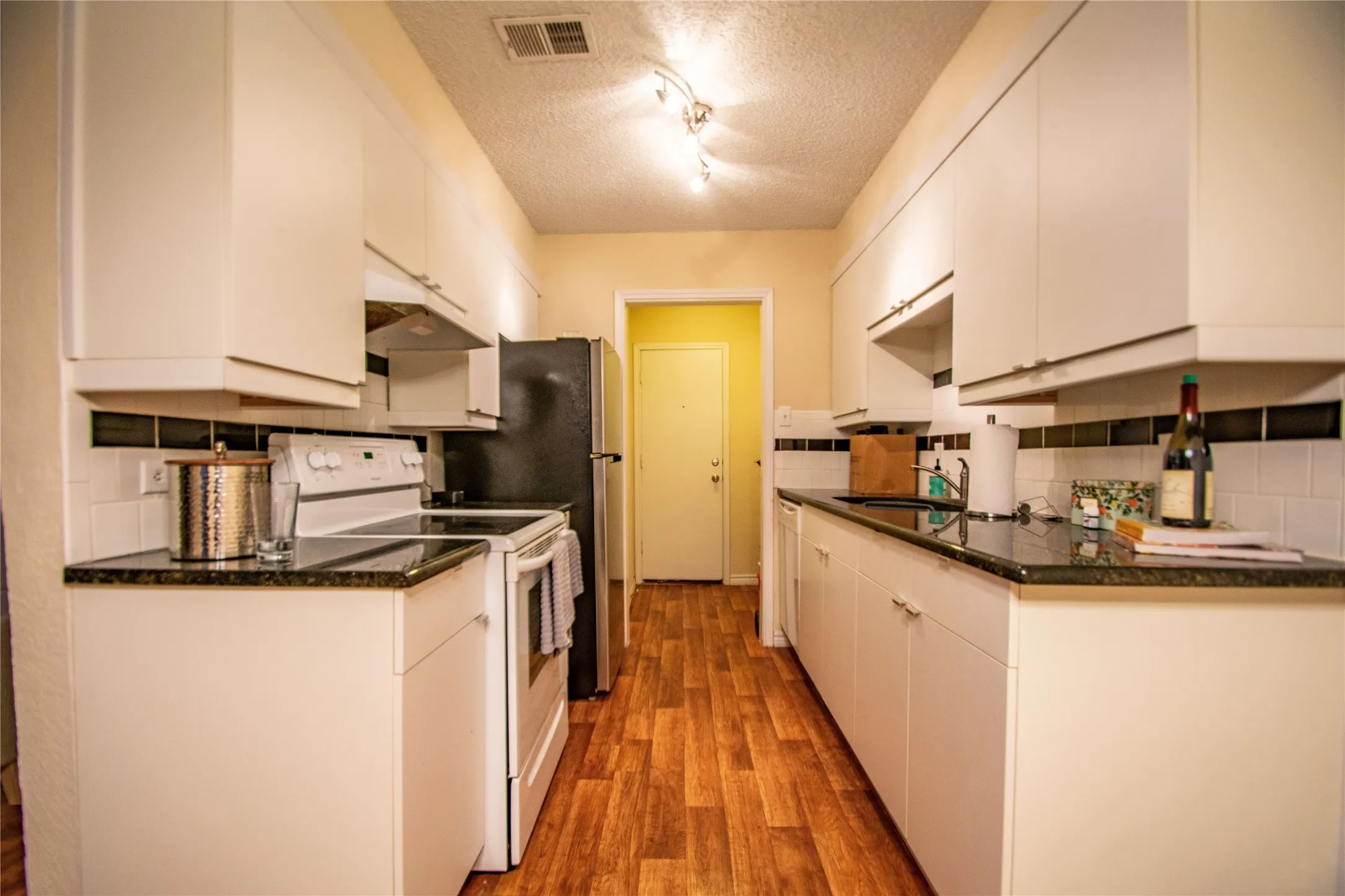 Kitchen featuring white cabinets, a textured ceiling, white electric range, and backsplash