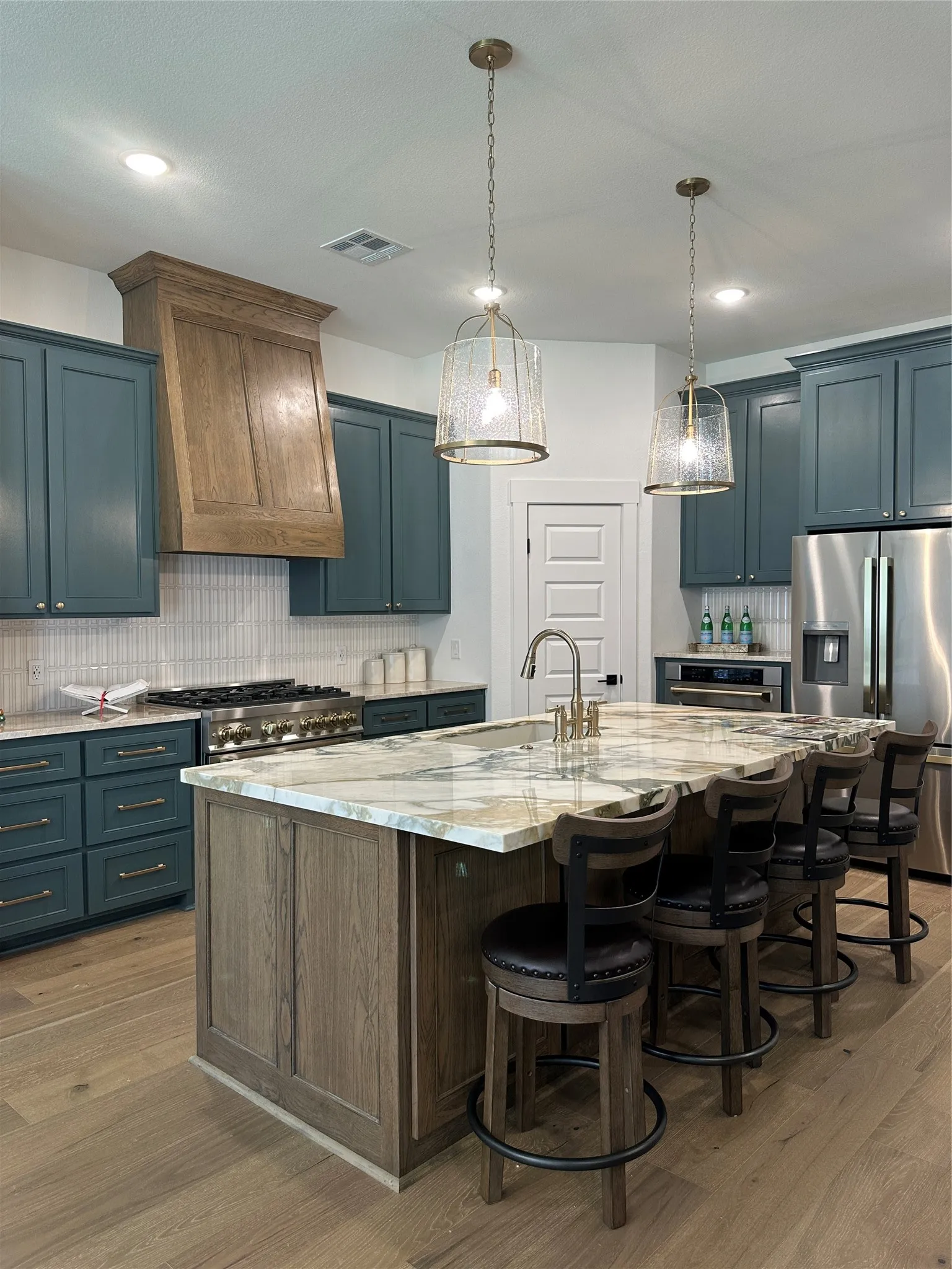 Gourmet kitchen featuring a large island with seating, a professional-grade range, stainless steel appliances, custom cabinetry, and wood-finish flooring