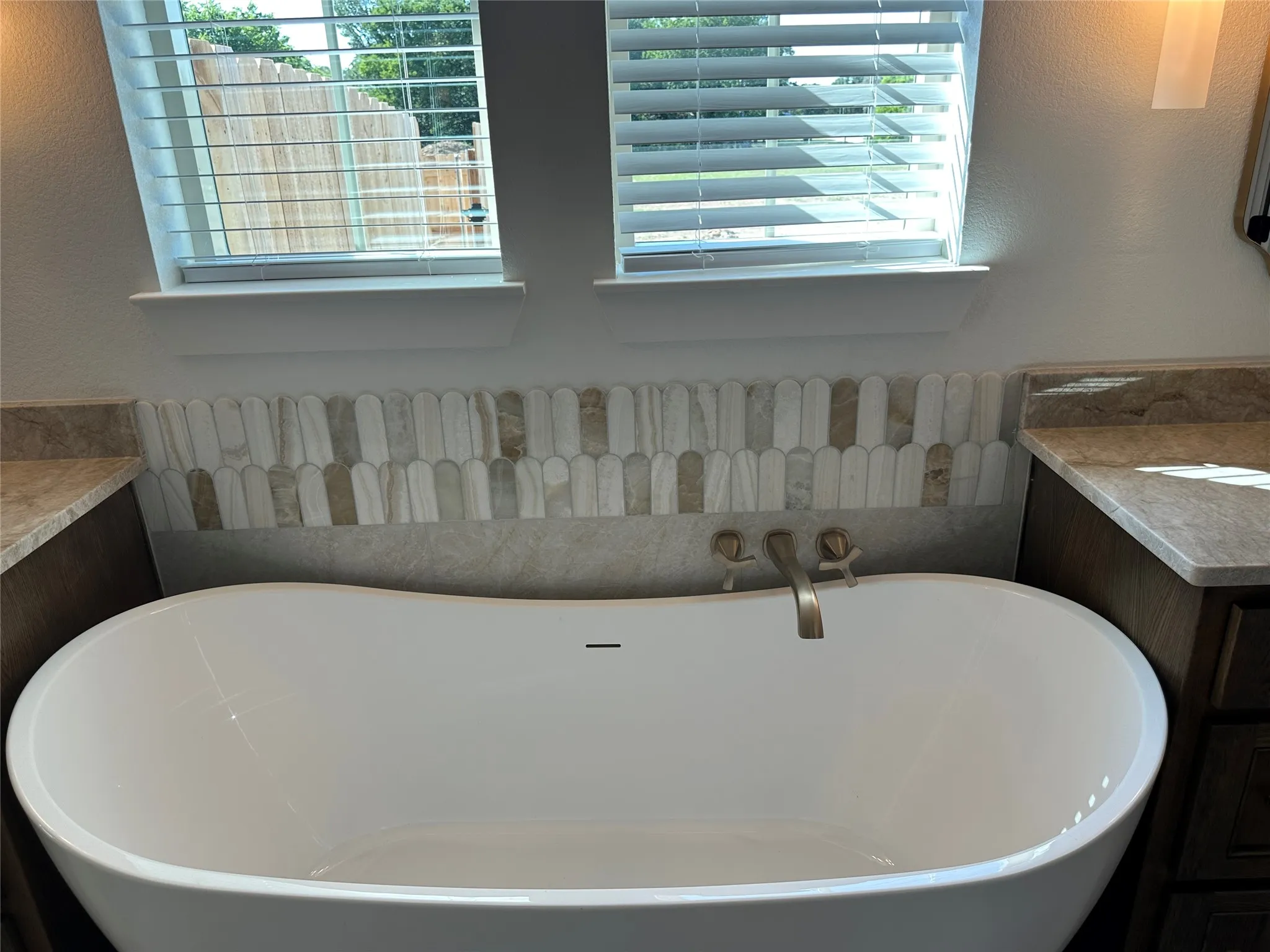Freestanding soaking tub with brushed nickel wall-mounted faucet, complemented by a decorative tile backsplash featuring an elongated picket pattern