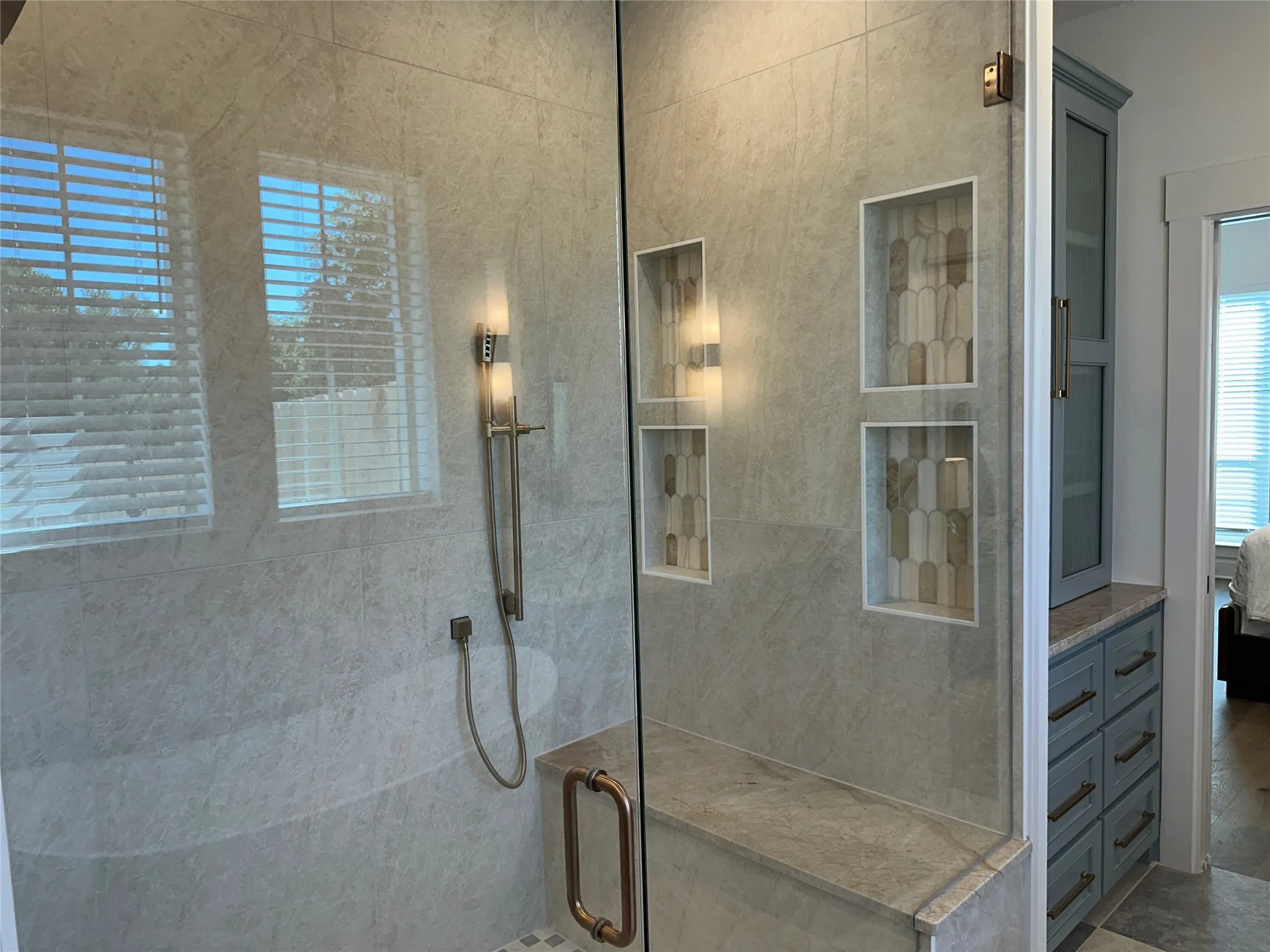 Glass-enclosed shower featuring large format tile, a built-in bench, two integrated display niches with decorative tile, and a handheld shower fixture
