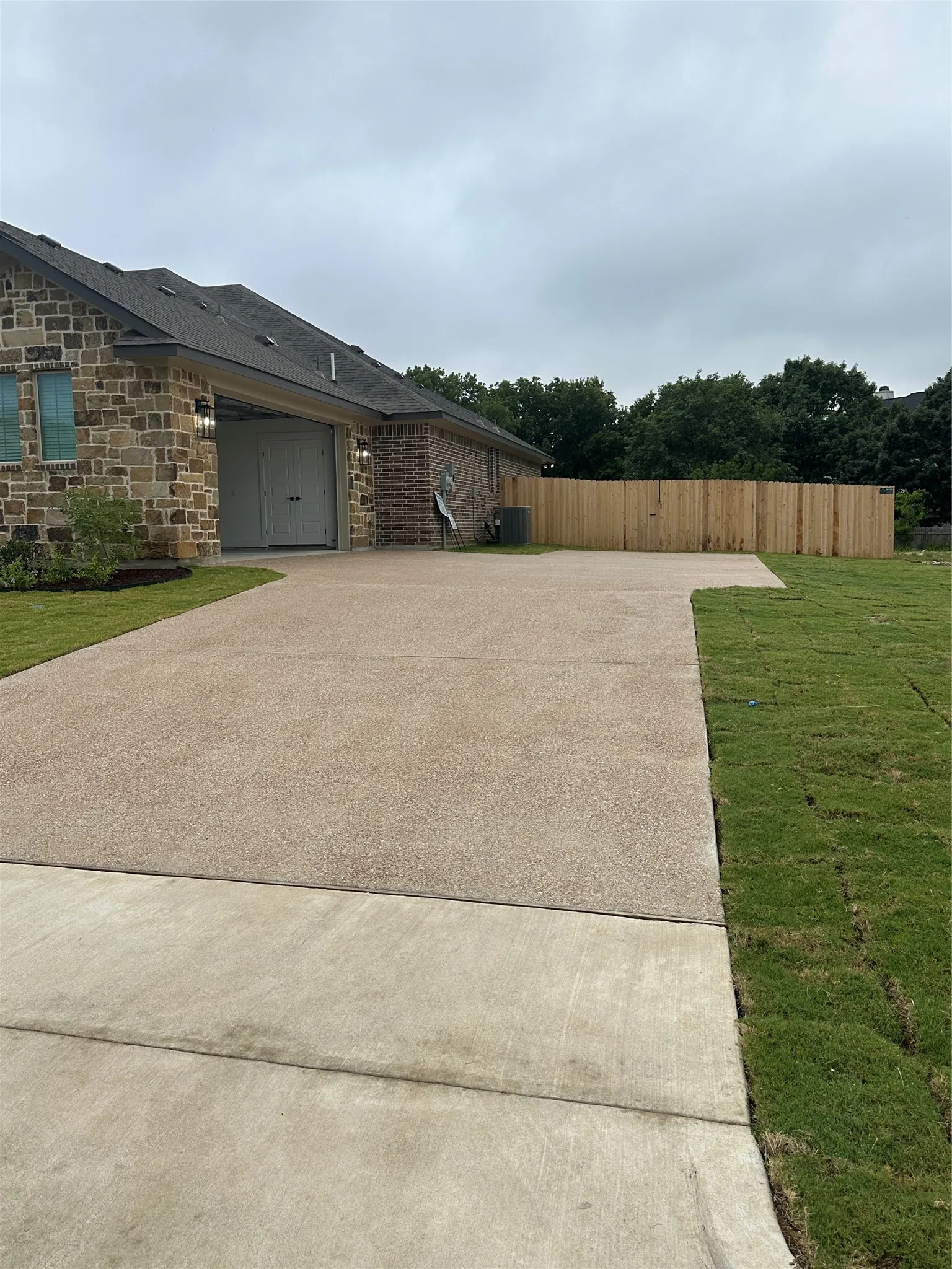 Expansive aggregate driveway featuring a two-car garage with overhead lighting