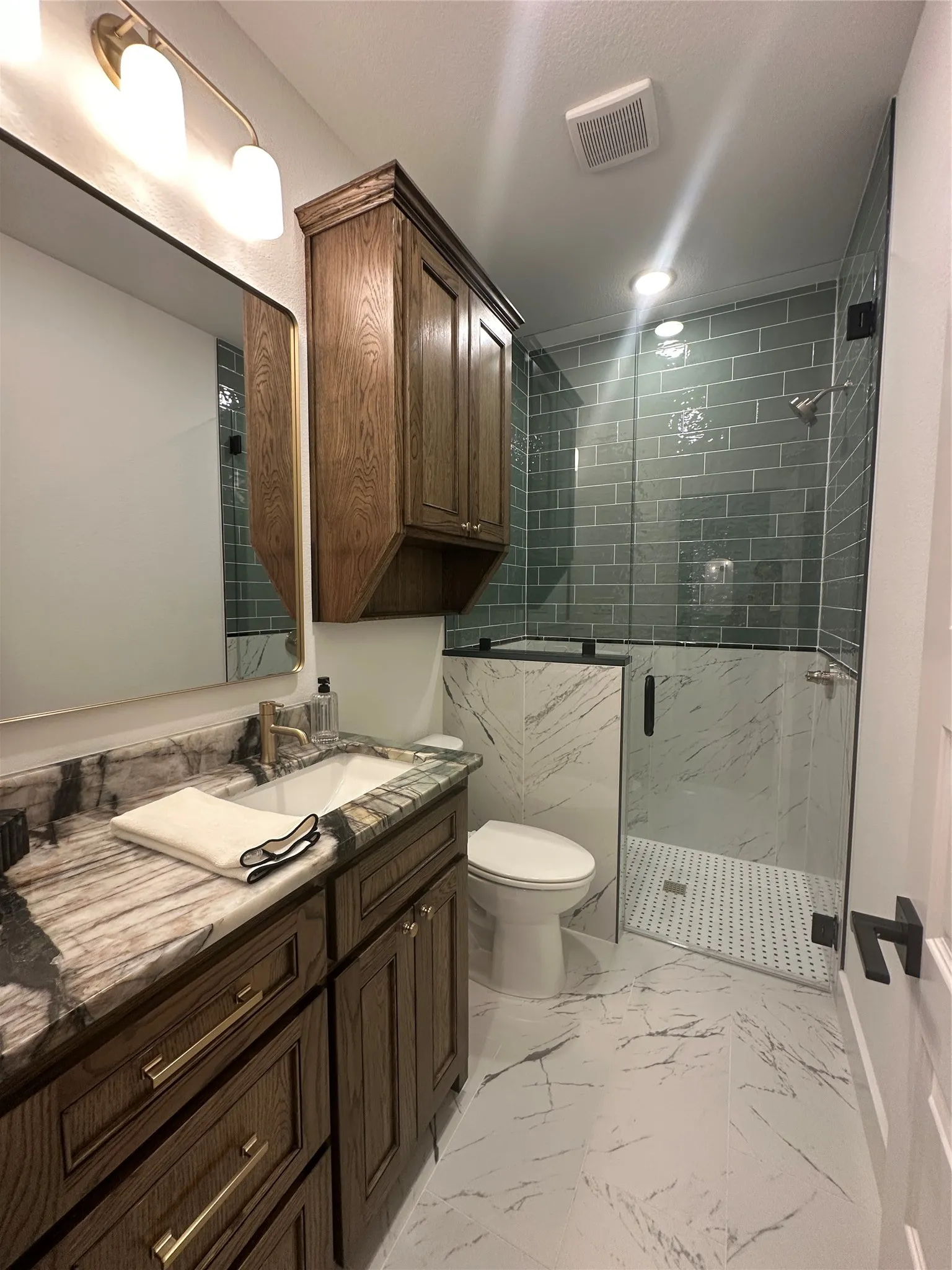 Bathroom featuring a dark wood-finish vanity with gold-tone hardware, a rectangular undermount sink, and a patterned stone countertop