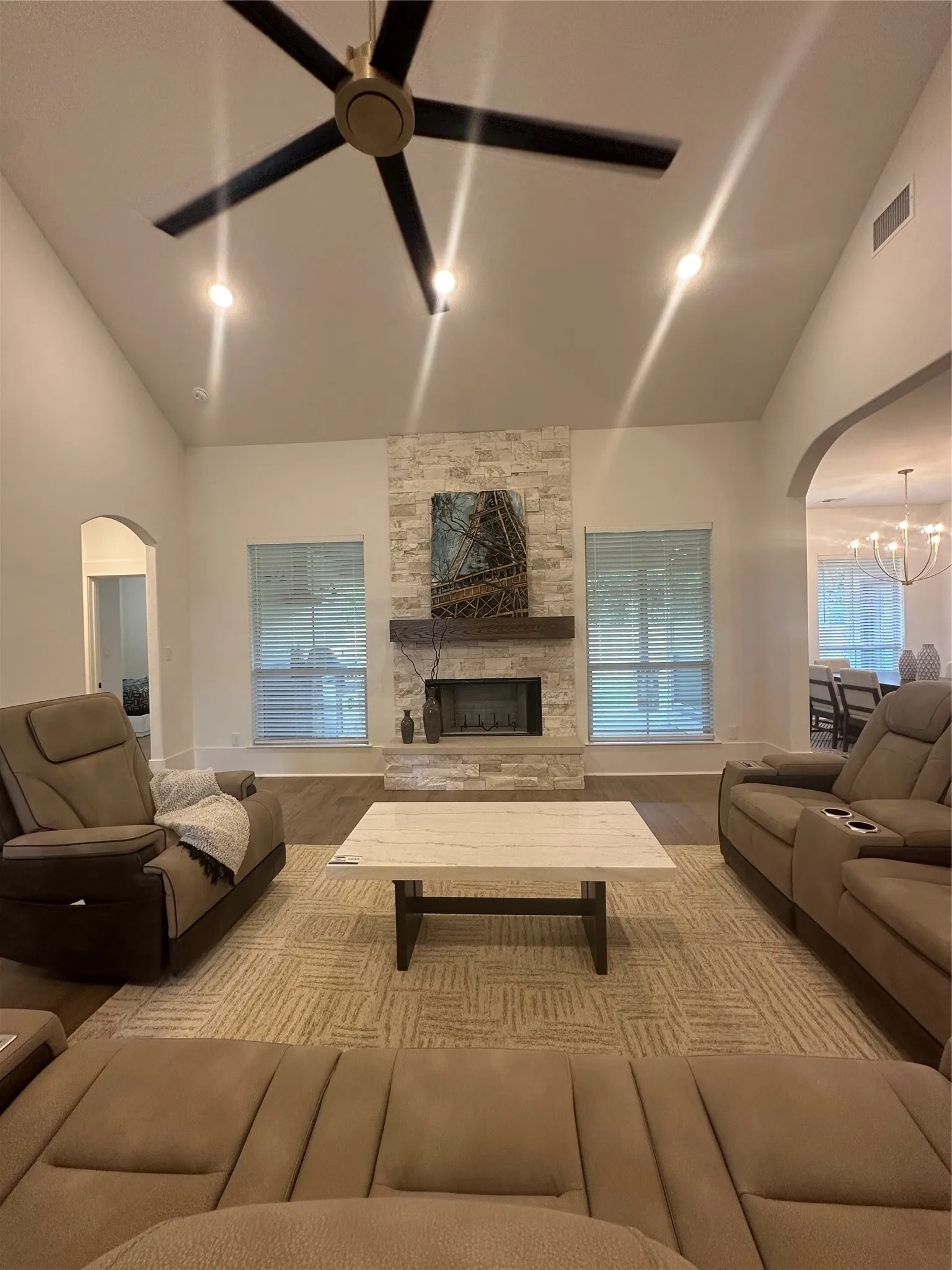 Vaulted ceiling living area featuring a stone fireplace with wood mantel, large windows, recessed lighting, and a ceiling fan