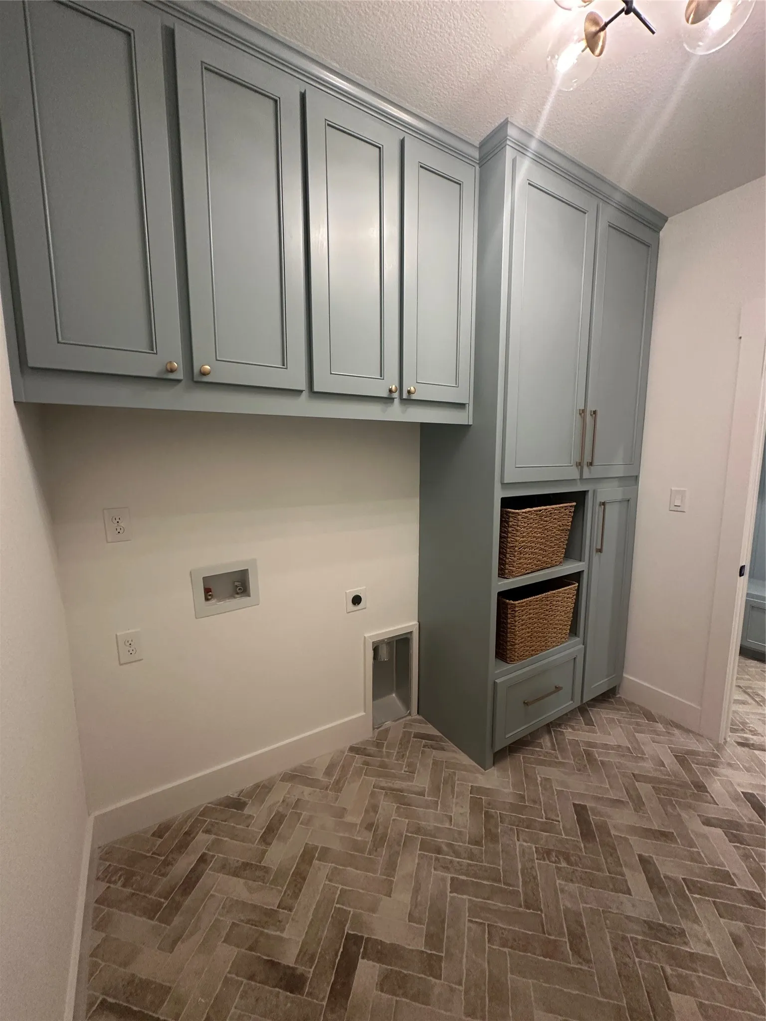 Laundry area featuring herringbone-patterned floor tiles, extensive cabinetry with crown molding, and modern light fixture