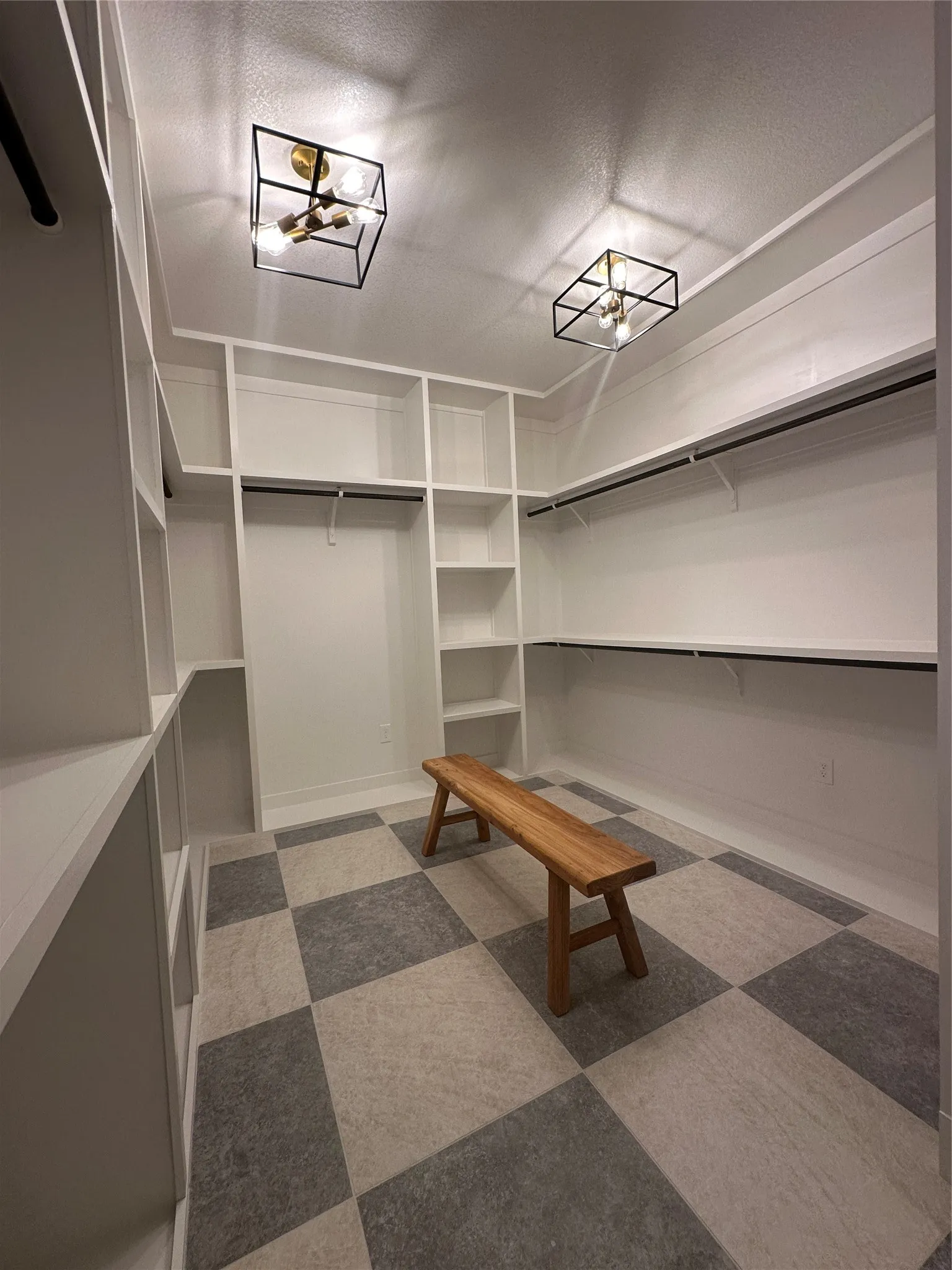 Spacious custom closet featuring extensive built-in shelving, hanging rods, two modern flush-mount light fixtures, and checkerboard pattern flooring