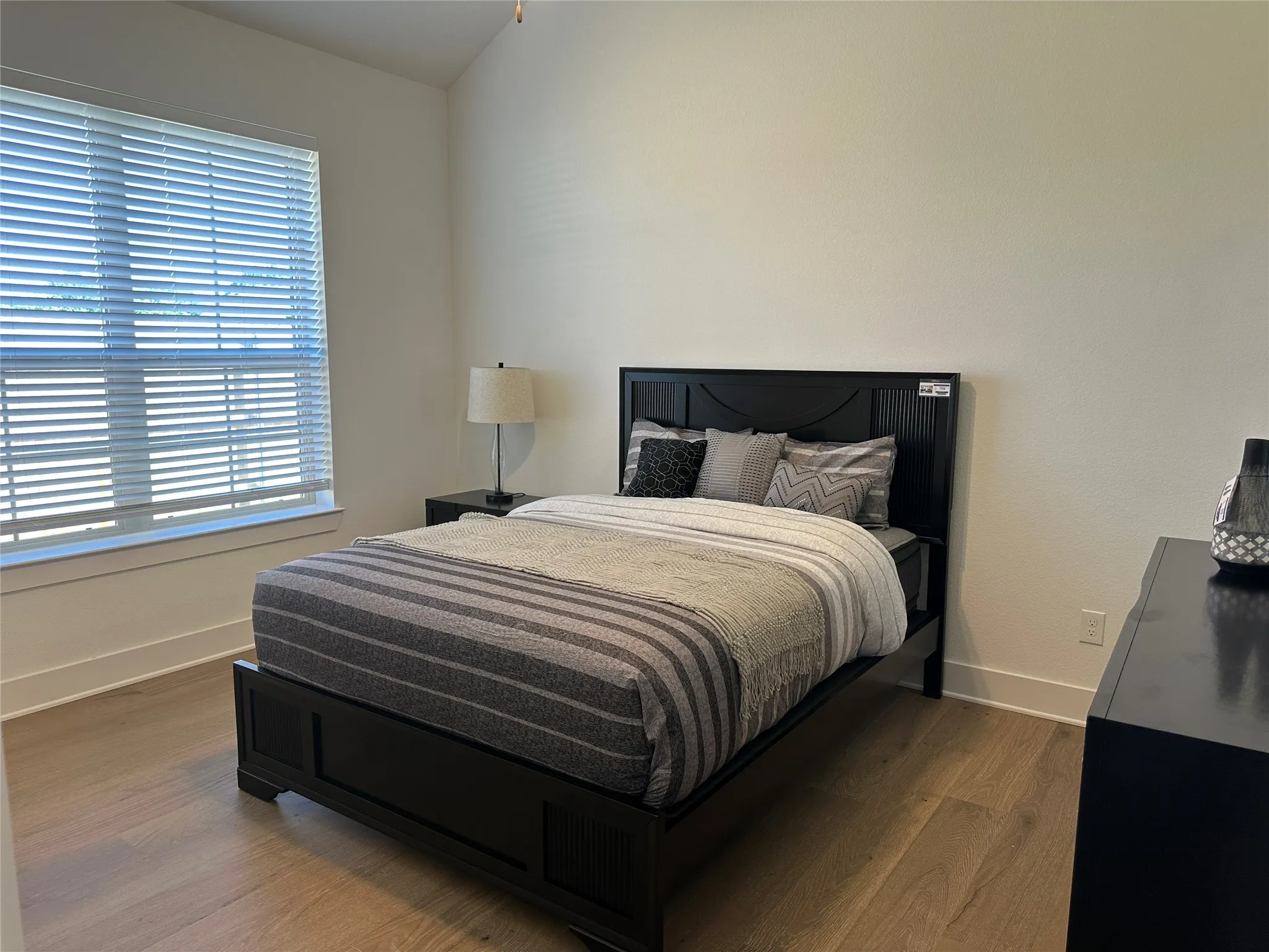 Room featuring wood-finish flooring, a vaulted ceiling, and ample natural light from a large window with blinds