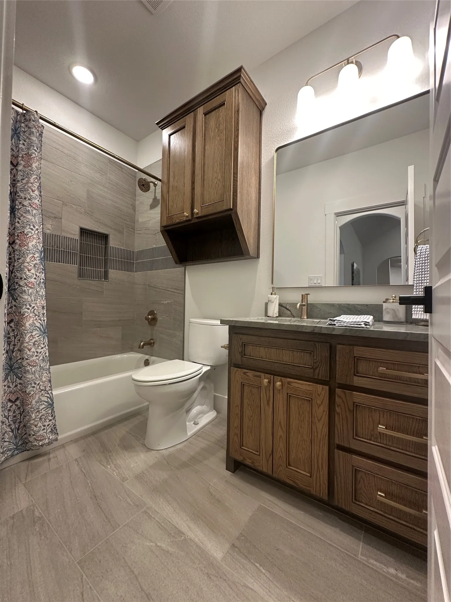 Bathroom featuring wood-finish vanity with countertop, large mirror, and three-light fixture