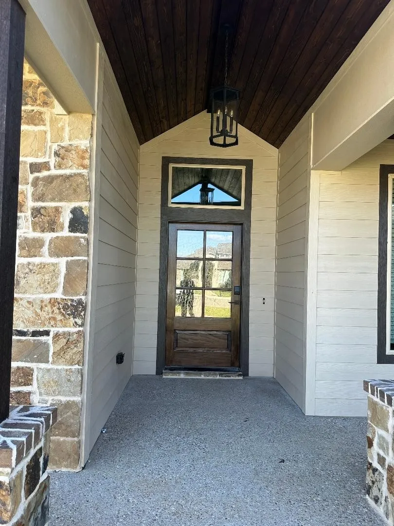 Covered entryway featuring a wood-paneled ceiling, stone column accents, and a wood-frame door with glass panels