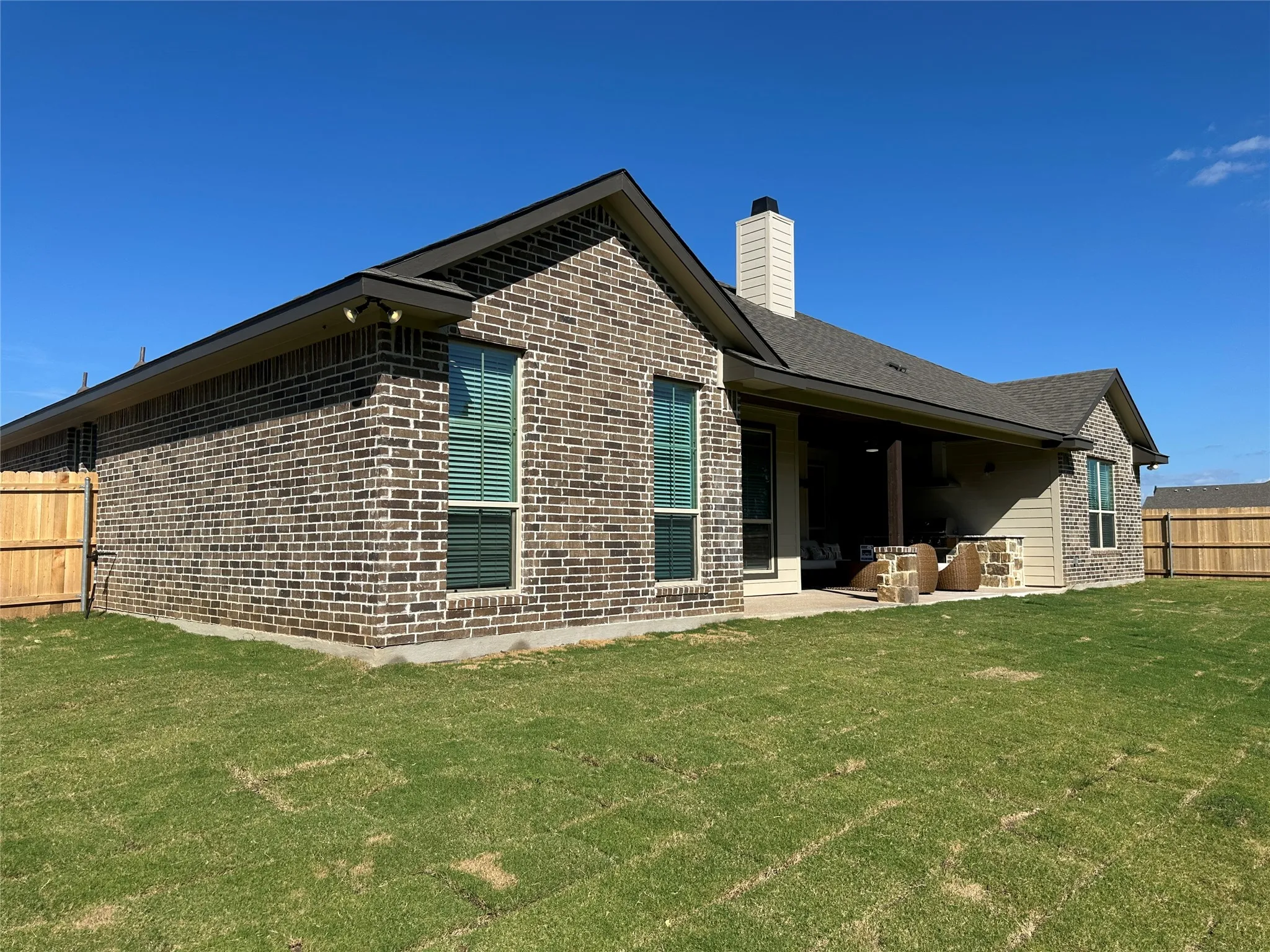 Spacious outdoor living area with a covered patio, brick and stone veneer exterior, and a large grassy yard