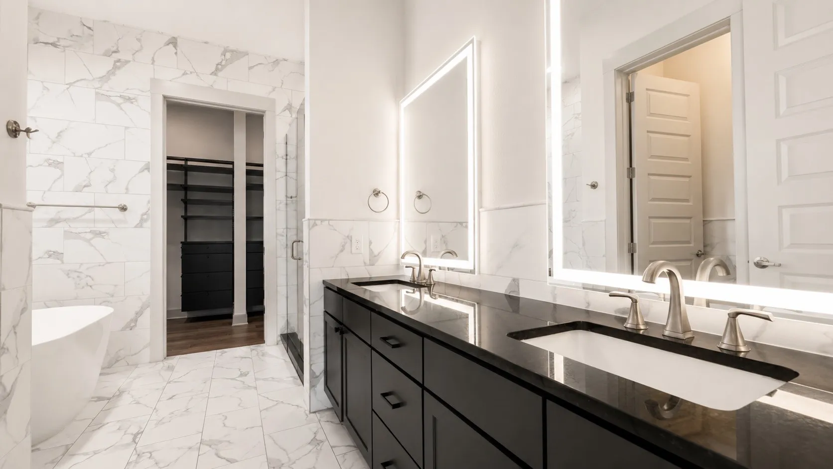 Double vanity with dark cabinetry, integrated sinks, and backlit mirrors