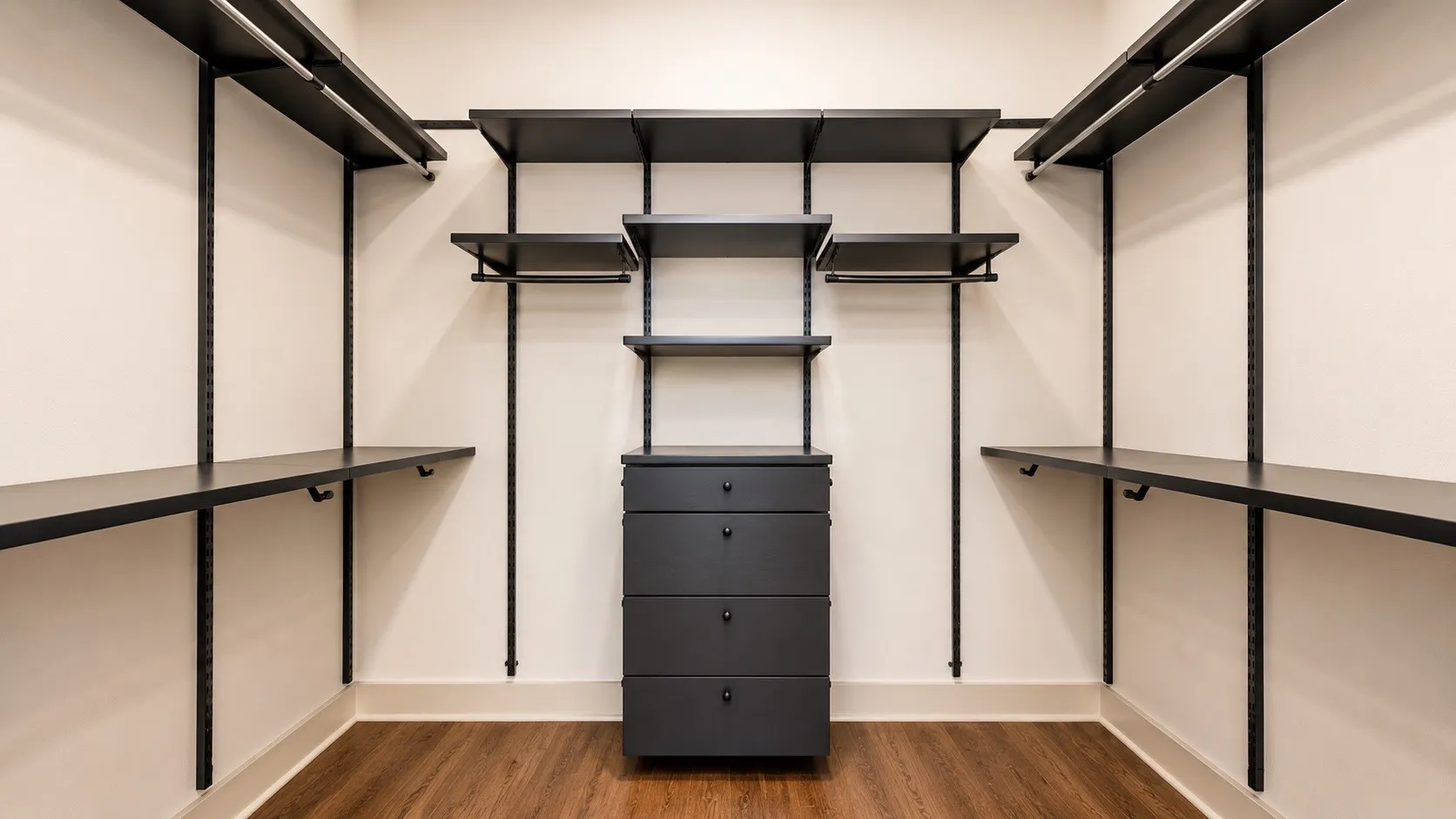 Custom closet system featuring dark wood-finish flooring, white walls, and a central five-drawer dresser