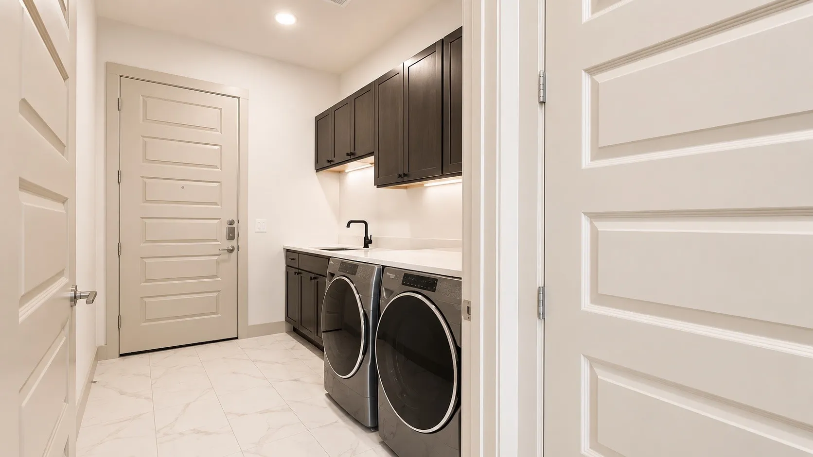 Utility room featuring dark wood-finish cabinetry, a sink with a matte black faucet, and light stone-look countertops