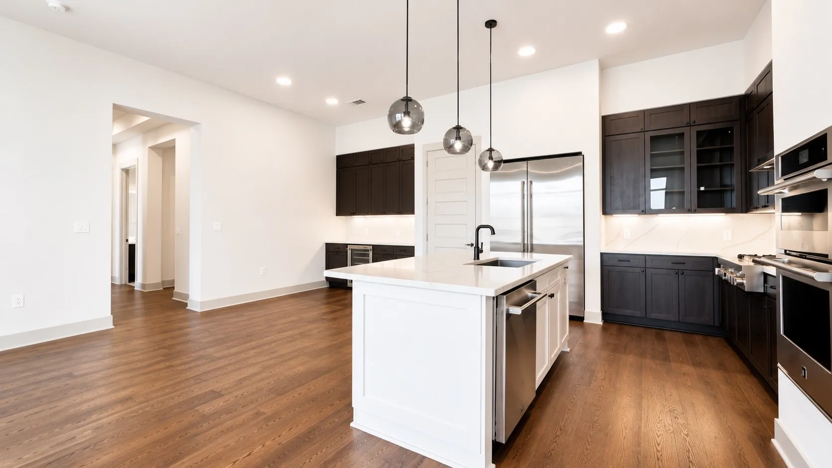 Gourmet kitchen featuring a central island with a white countertop and seating, dark wood-finish cabinetry, stainless steel appliances, and wood-finish flooring