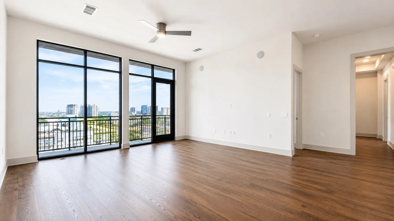 Expansive window wall with black frames, a sliding glass door to an outdoor balcony, and cityscape scenery