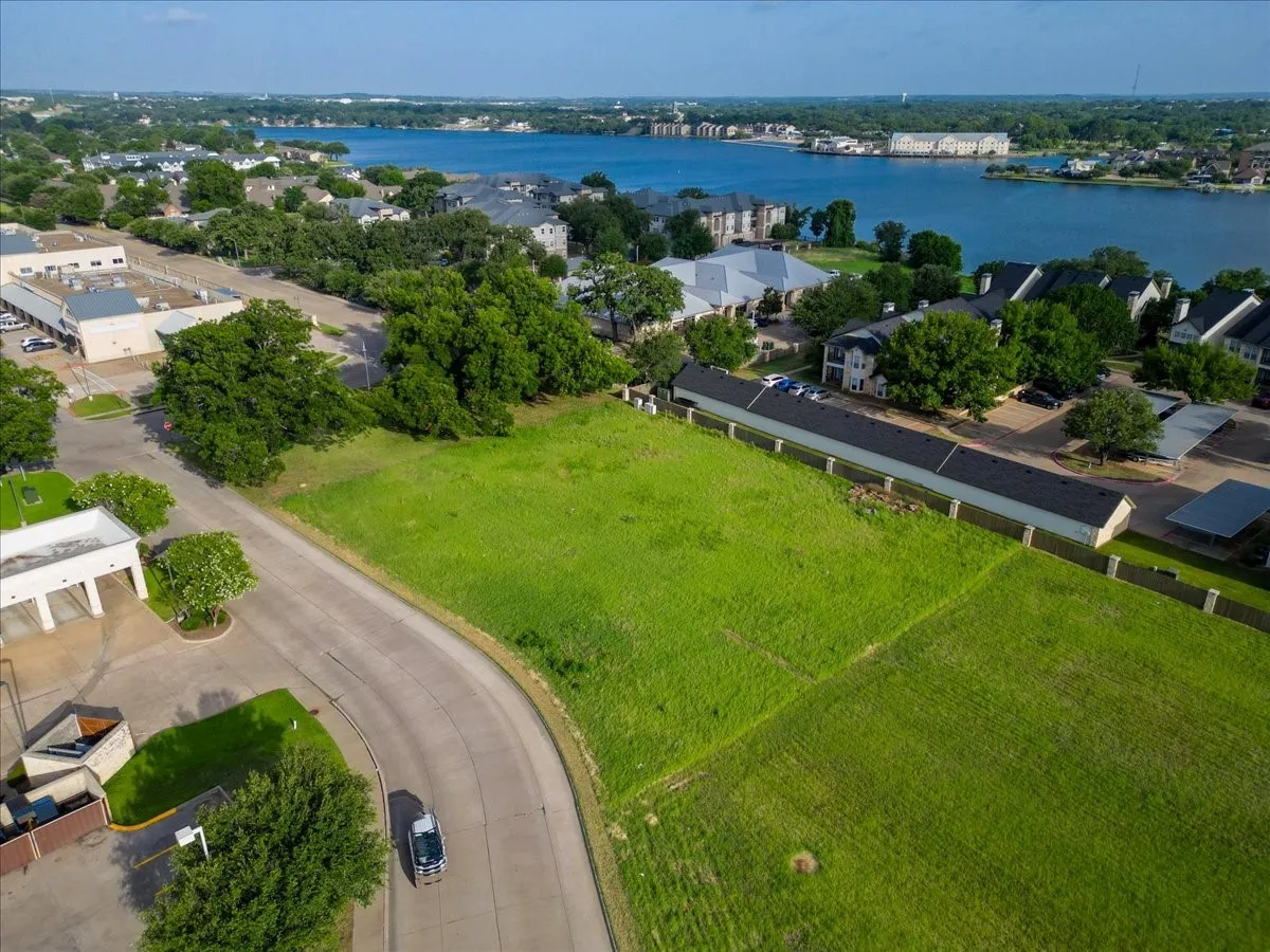 Expansive green lot with established perimeter fencing, featuring a curved paved roadway