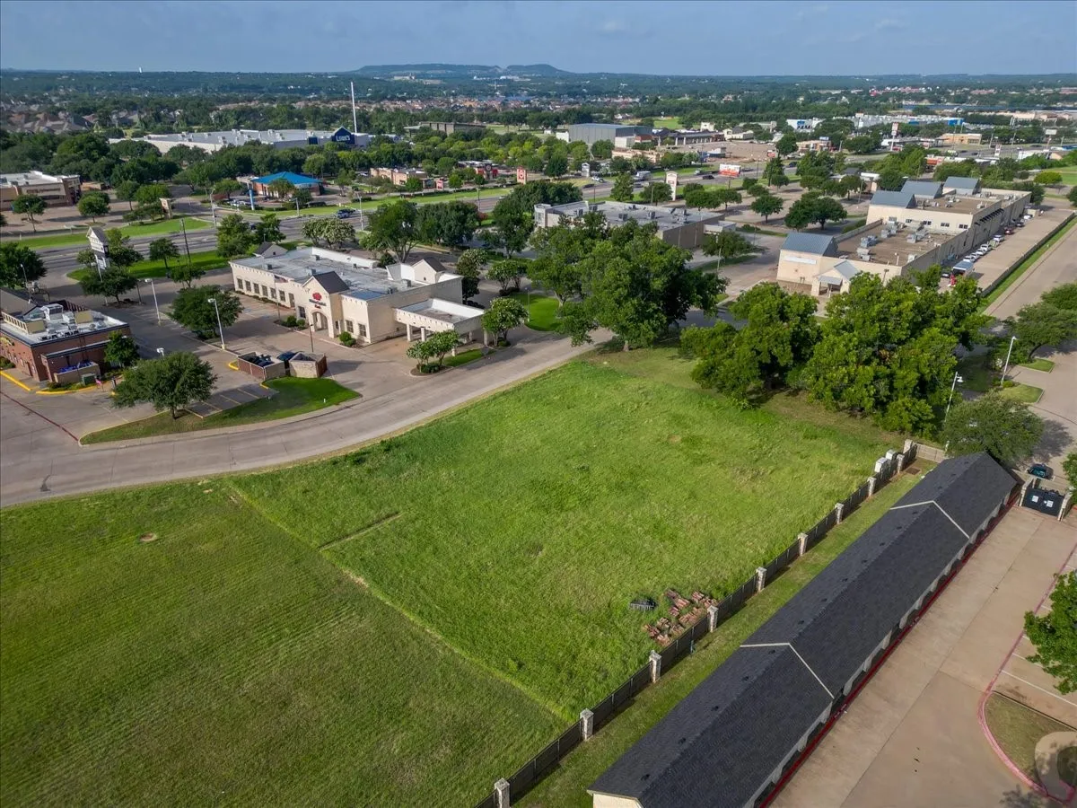Expansive grassy lot bordered by a concrete-capped fence on one side and a paved roadway on another