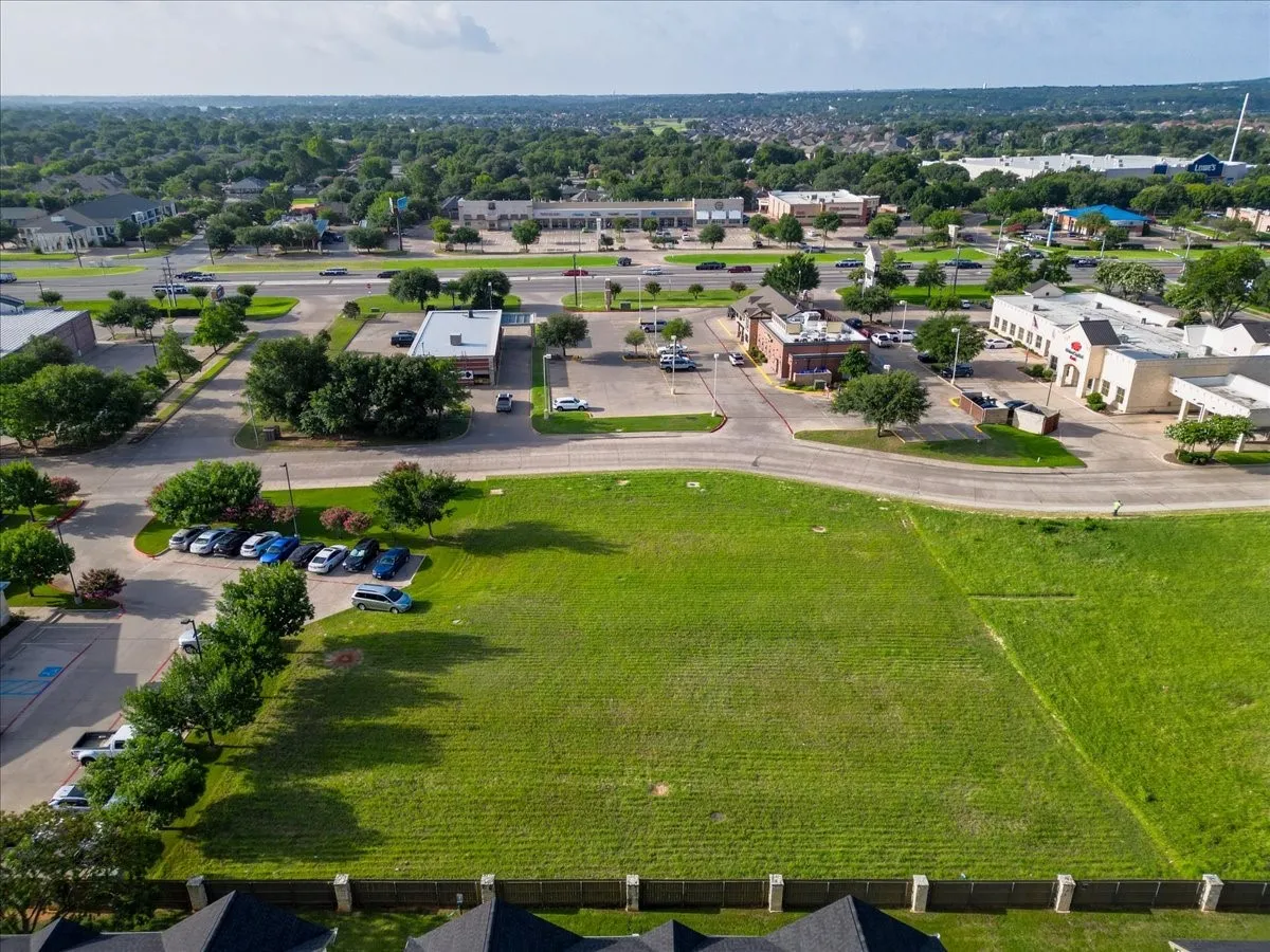 Expansive grassy lot bordered by a concrete fence and mature trees