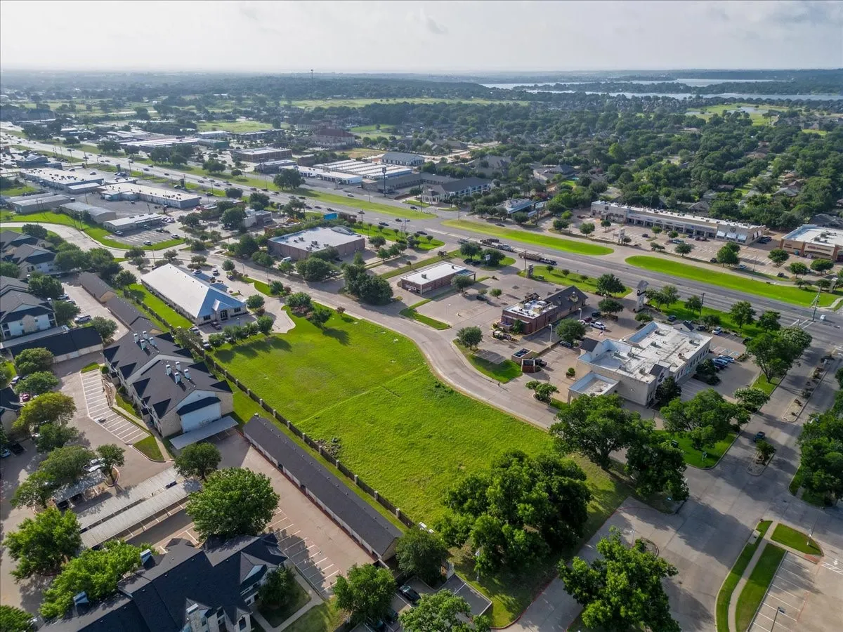 Expansive green space featuring road frontage, surrounded by commercial and multi-family properties, with a visible body of water in the distance
