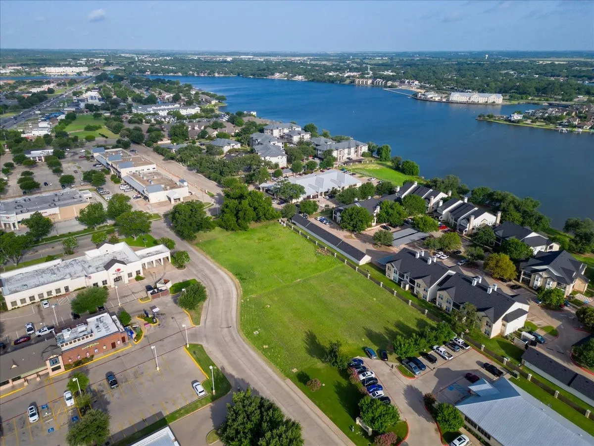 Expansive green lot featuring waterfront proximity, surrounding commercial buildings, established residential developments, and mature trees