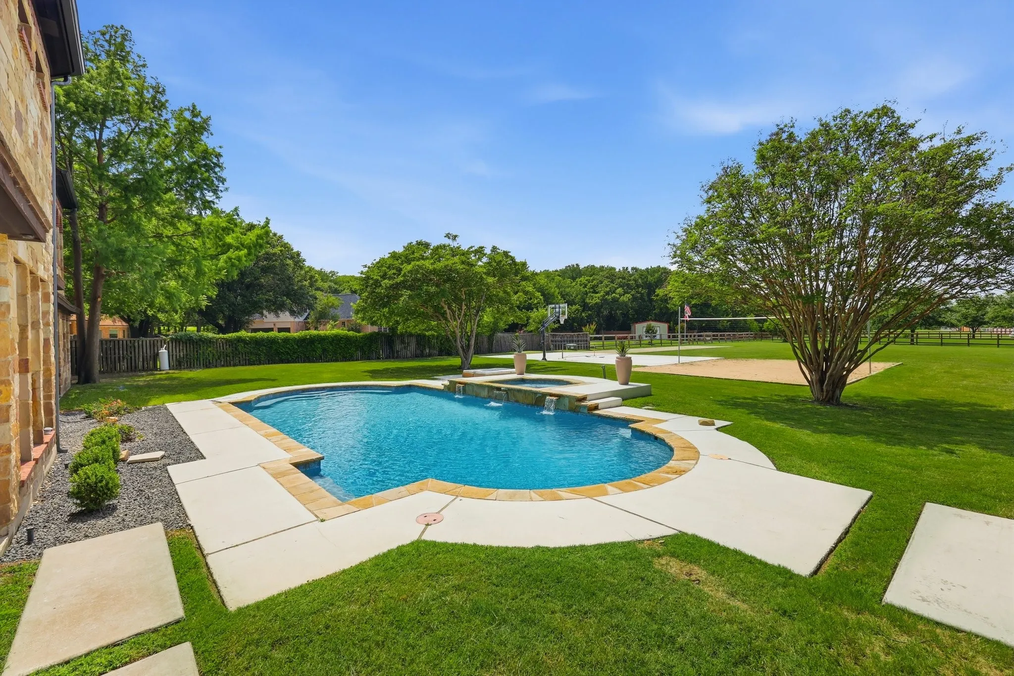 210 Canyon Oaks, Argyle, TX 76226 - Pool - Curved swimming pool featuring an integrated spa with waterfall, surrounded by concrete decking and stone coping