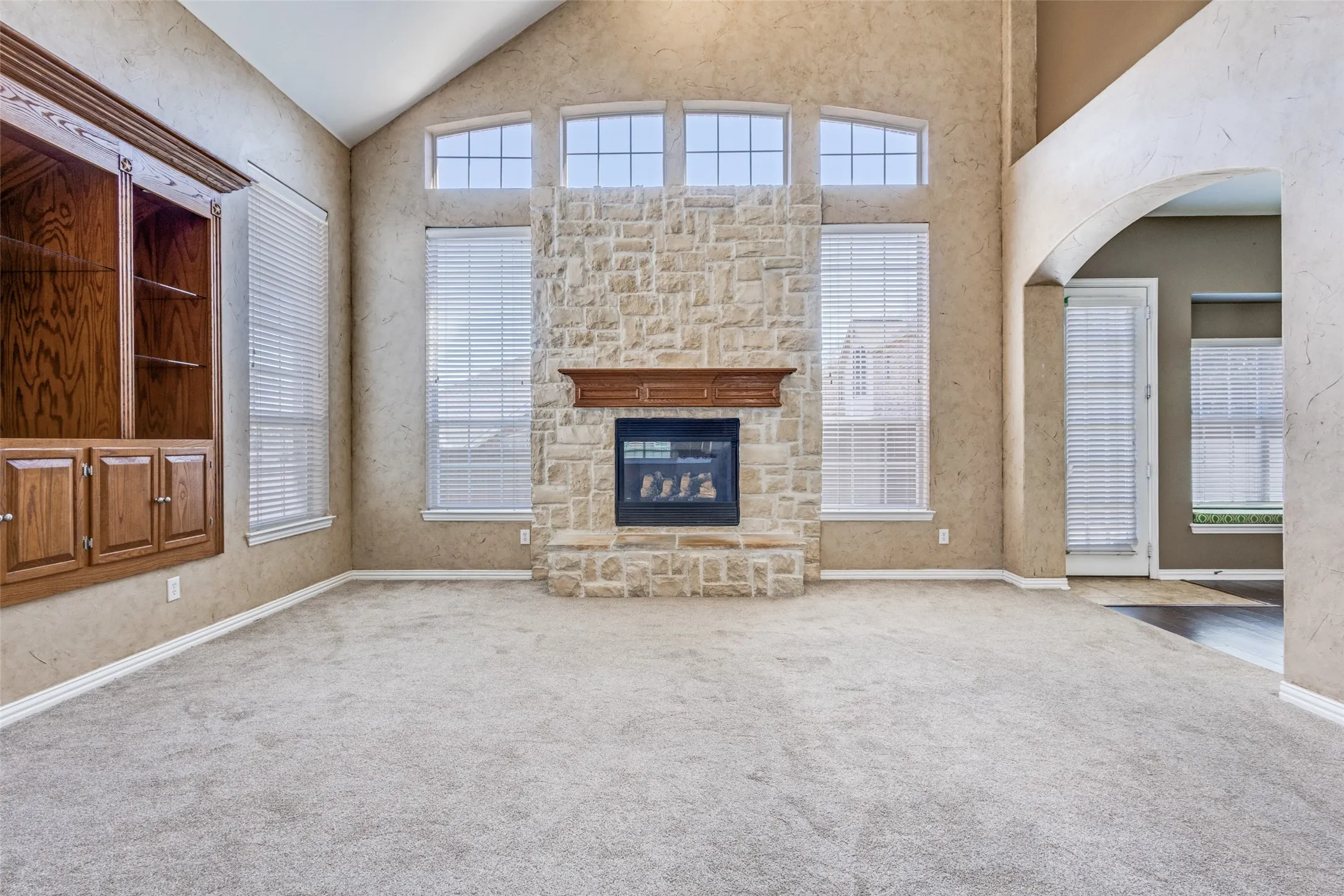 Expansive living room featuring a stone fireplace, arched walkways, abundant natural light, lofted ceiling, and a spacious layout, creating the perfect main gathering space for buyers searching for a McKinney Texas home with fireplace, open living area, and elegant traditional design in Virginia Woods near McKinney ISD schools.