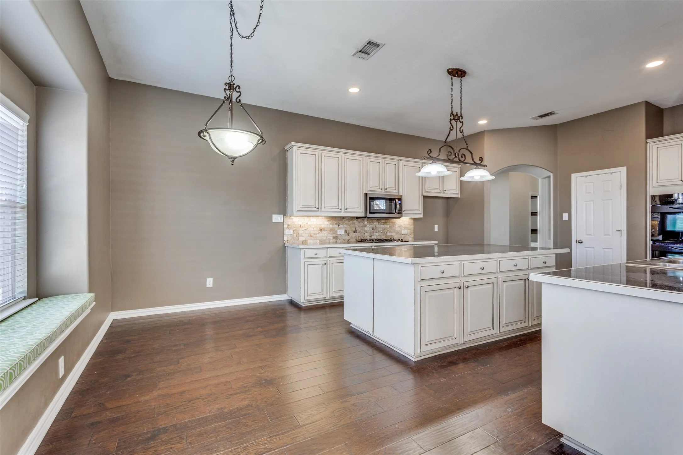 Kitchen detail view with island, dark wood flooring, backsplash, stainless steel microwave, and decorative light fixtures, highlighting the upgraded finishes, functional layout, and stylish design that today’s McKinney homebuyers want when searching for a move-in-ready home in Virginia Woods, McKinney ISD, and the greater DFW area.