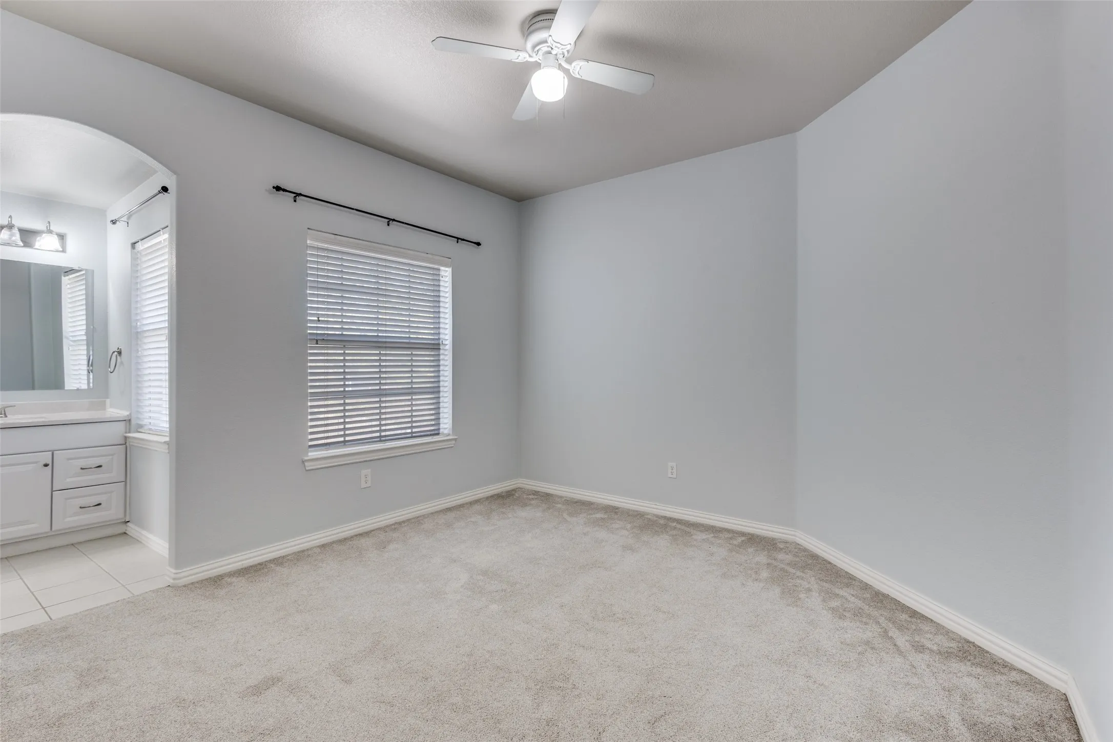 Spacious secondary bedroom with arched walkways, light carpet, ensuite bath access, and ceiling fan, ideal for buyers searching for a 4 bedroom McKinney TX home with comfortable guest space, family functionality, and a desirable floor plan in the Virginia Woods neighborhood near schools, shopping, and commuter routes.