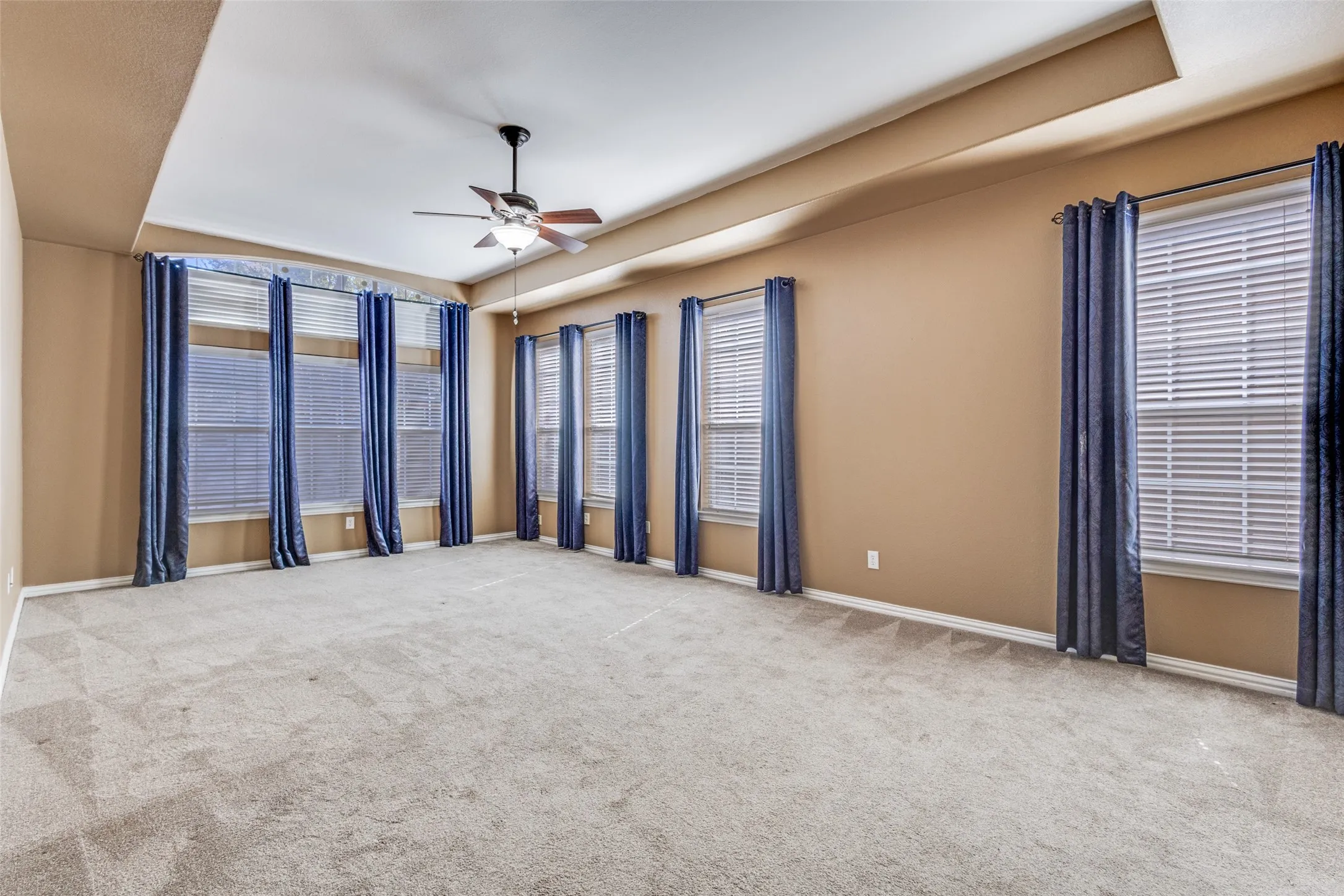 Unfurnished room with ceiling fan, light carpet, and a tray ceiling