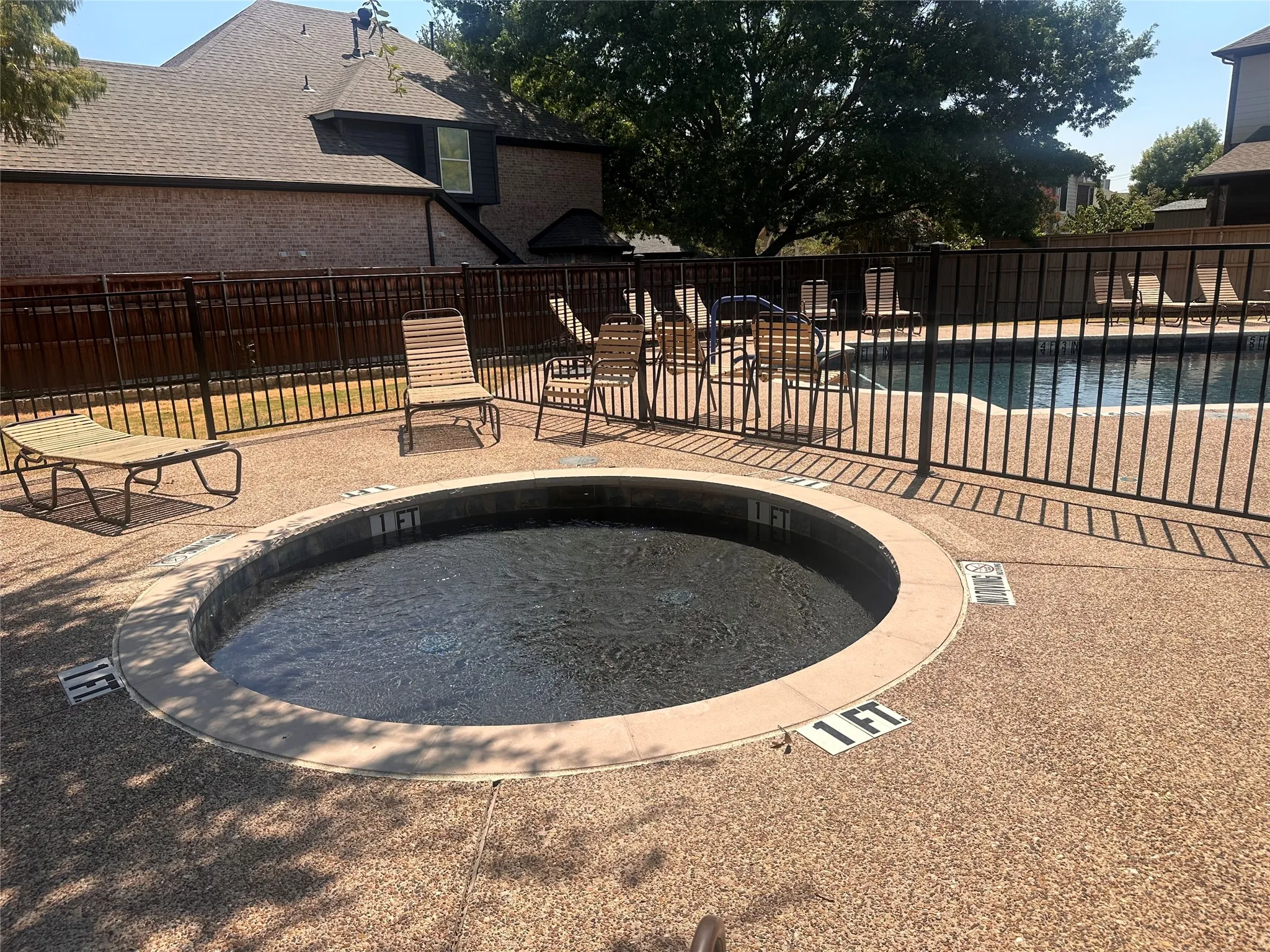 Circular spa with aggregate decking, surrounded by a metal fence enclosure