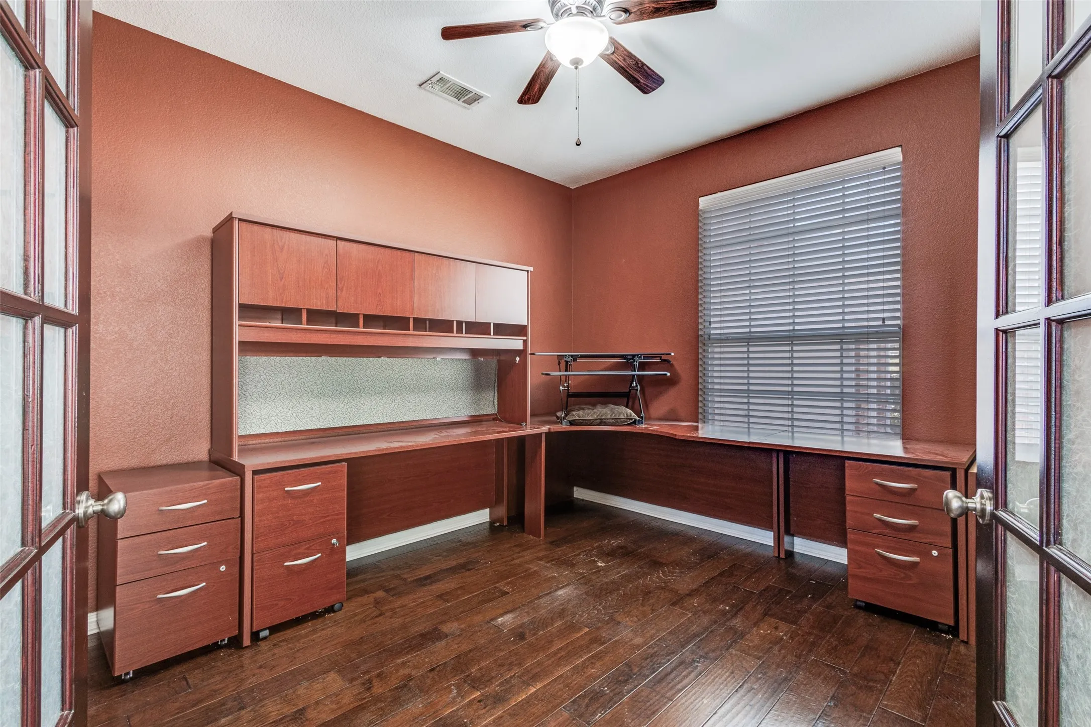 Dedicated office with dark wood-style flooring, built-in study area, ceiling fan, and textured accent wall, creating a private and functional work-from-home environment that is highly desirable for buyers searching for a McKinney home with office, flexible floor plan, and strong commuter convenience near Highway 75 and Highway 380.