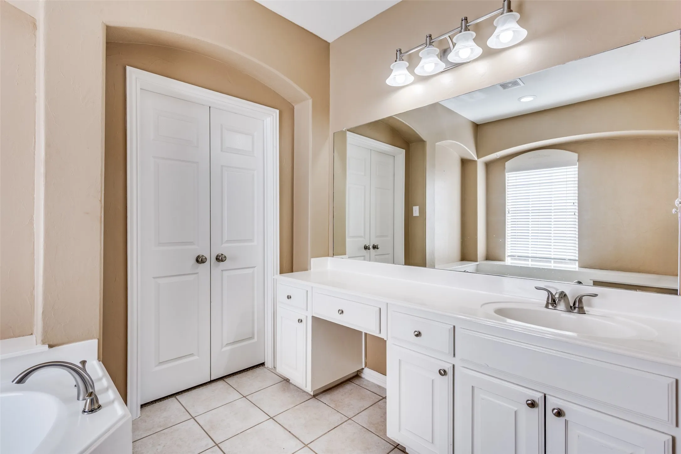 Primary-style bathroom with garden tub, vanity, light tile-patterned floors, and closet space, delivering an inviting owner’s suite feel that appeals to buyers searching for a McKinney Texas home with spa-inspired bath features, traditional design, and a comfortable first-floor primary retreat.