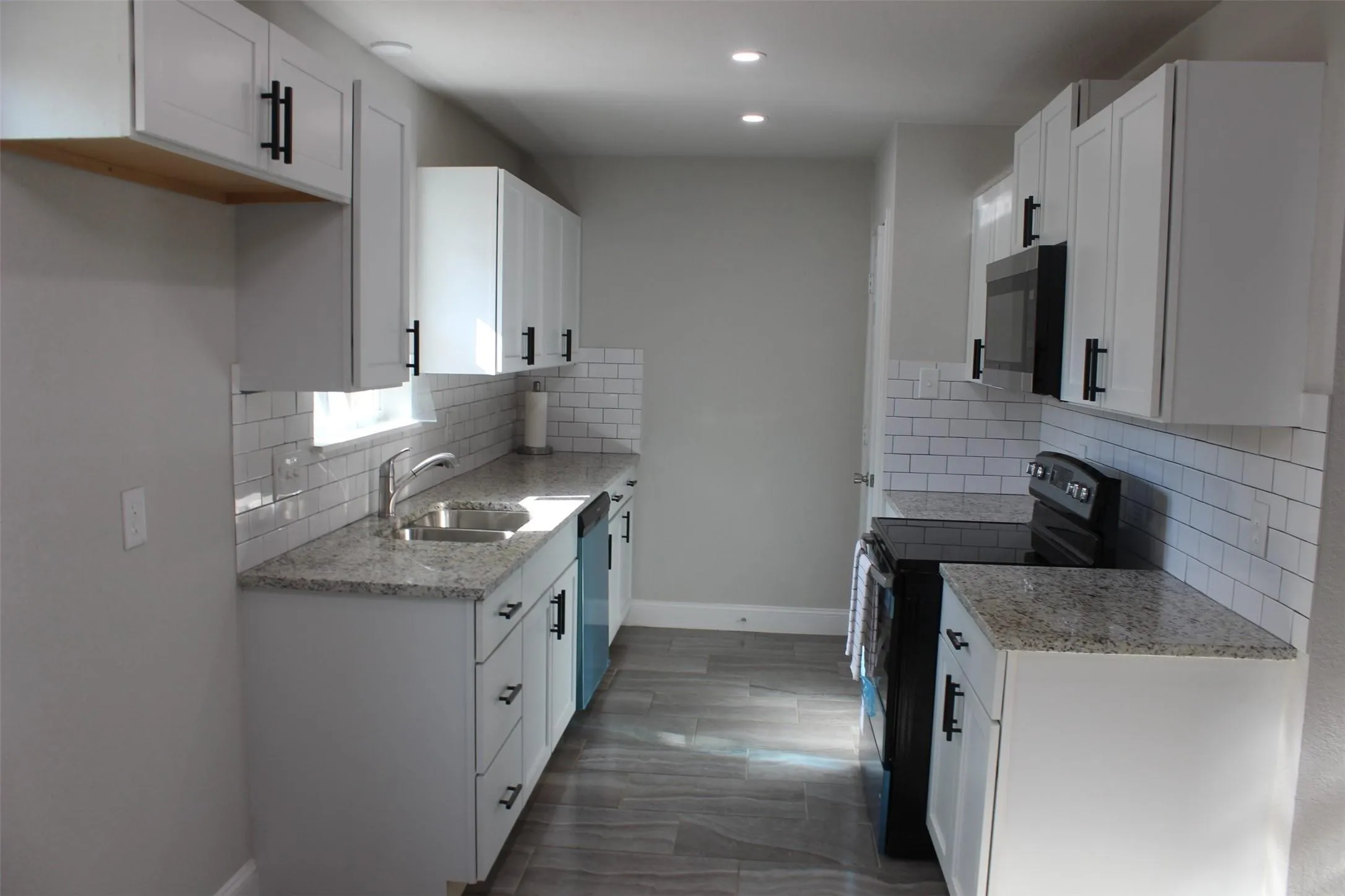 Modern kitchen featuring white shaker cabinetry, granite countertops, subway tile backsplash, stainless steel sink, and wood-finish flooring